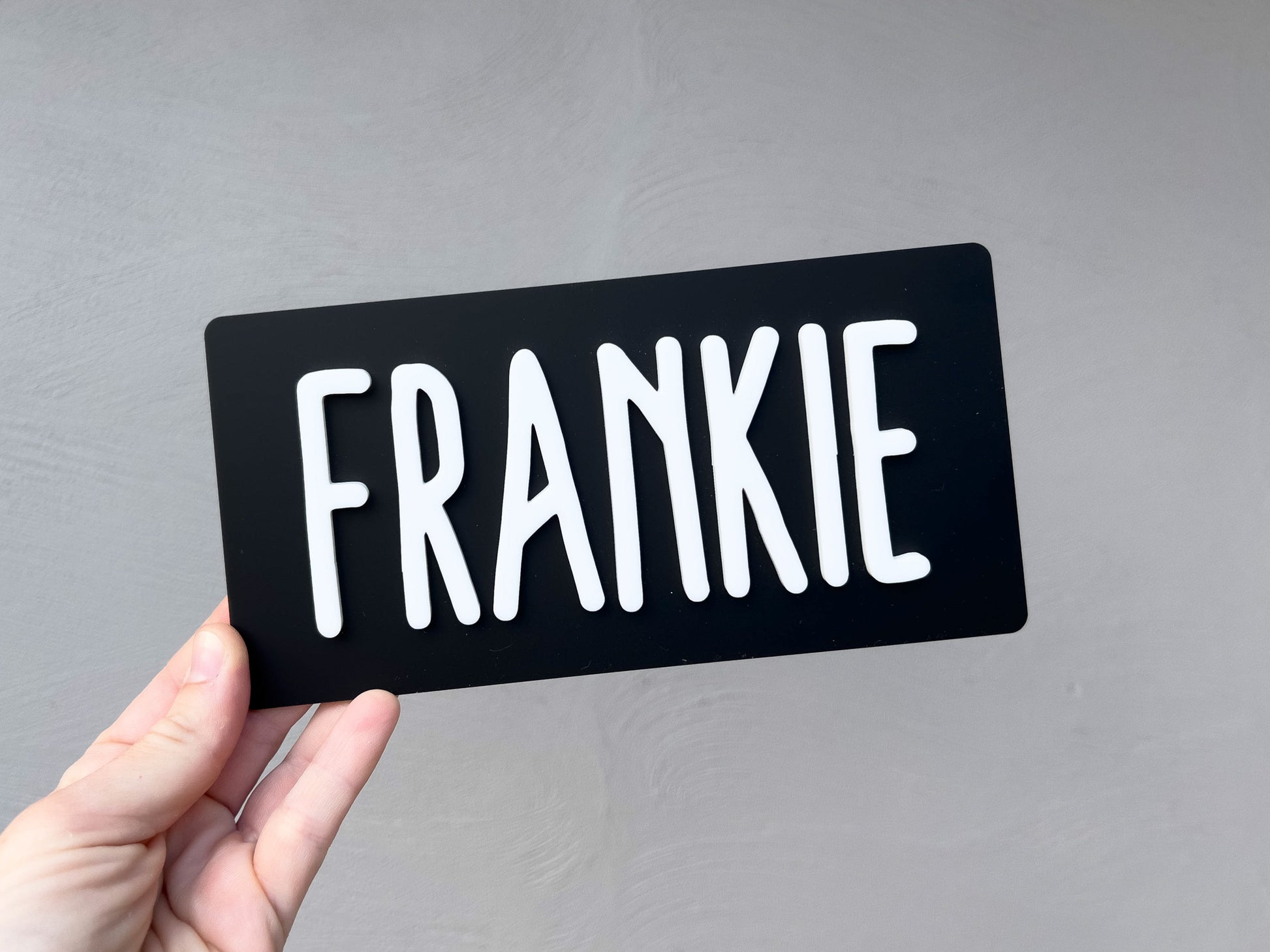 Black acrylic mini name plaque with 'FRANKIE' in white on a gray background