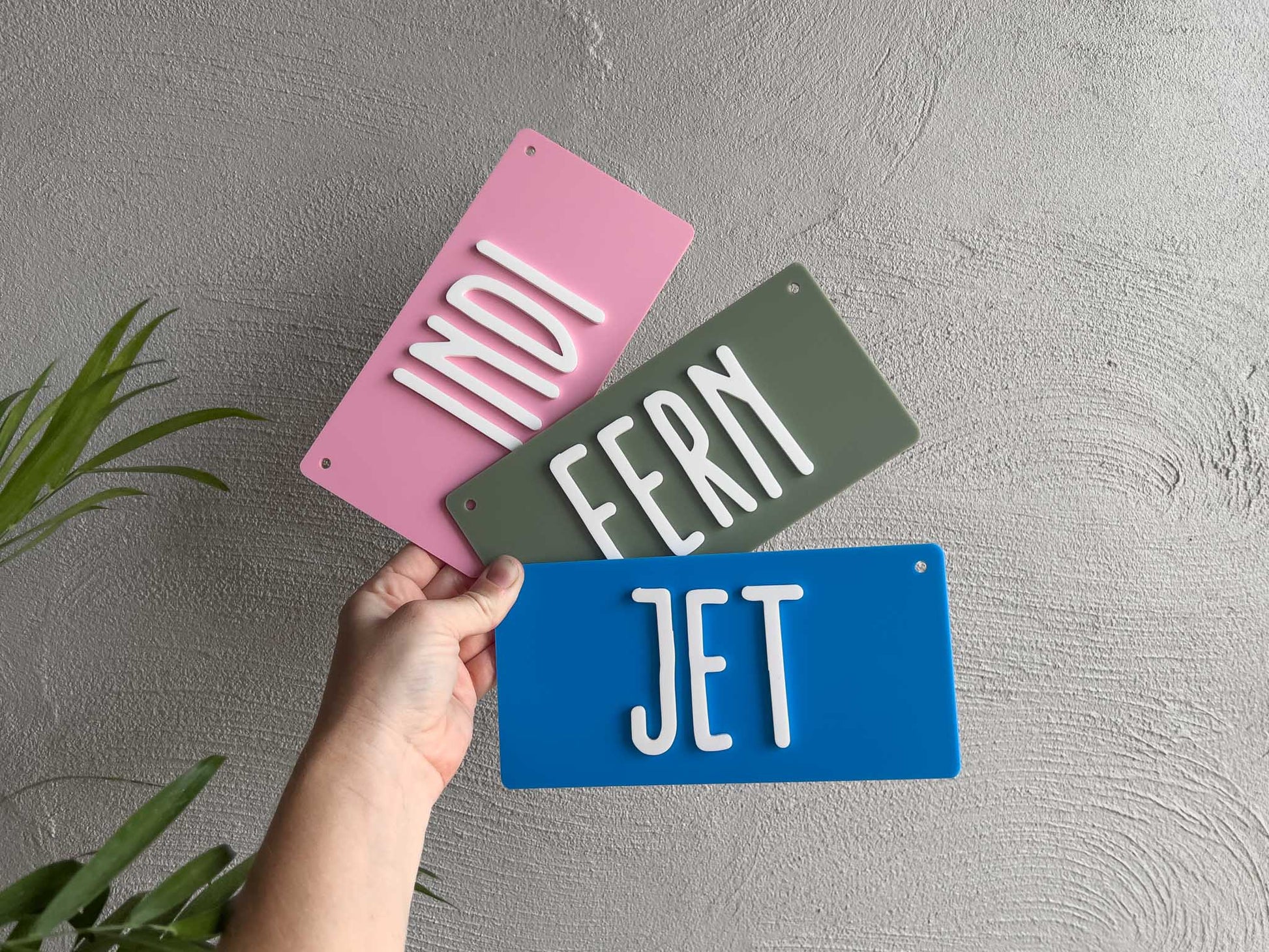 Three colorful name plate signs held by a hand against a gray background.