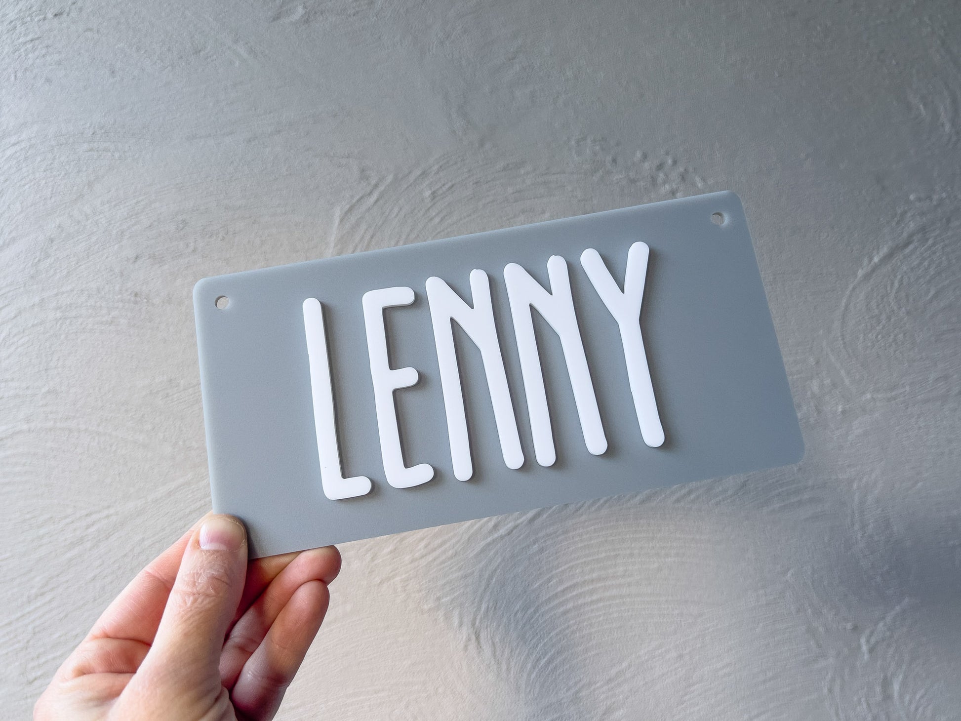 Hand holding a gray rectangular sign with 'LENNY' in white letters against a light gray background | Coji Designs