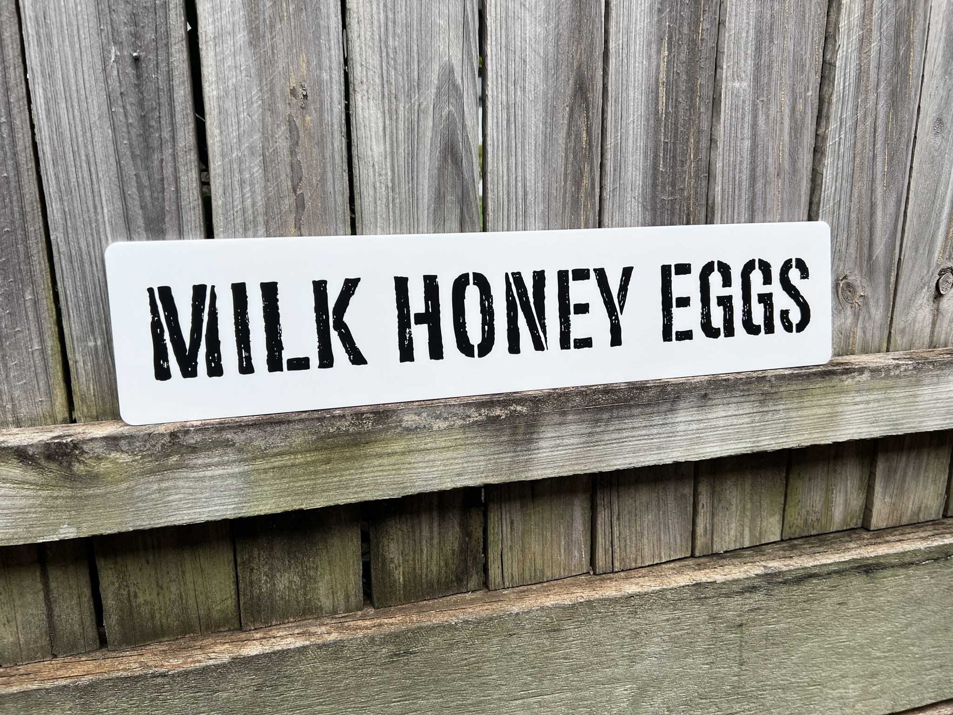 Custom printed vintage style signage with a distressed stencil style typography that says 'MILK HONEY EGGS'.