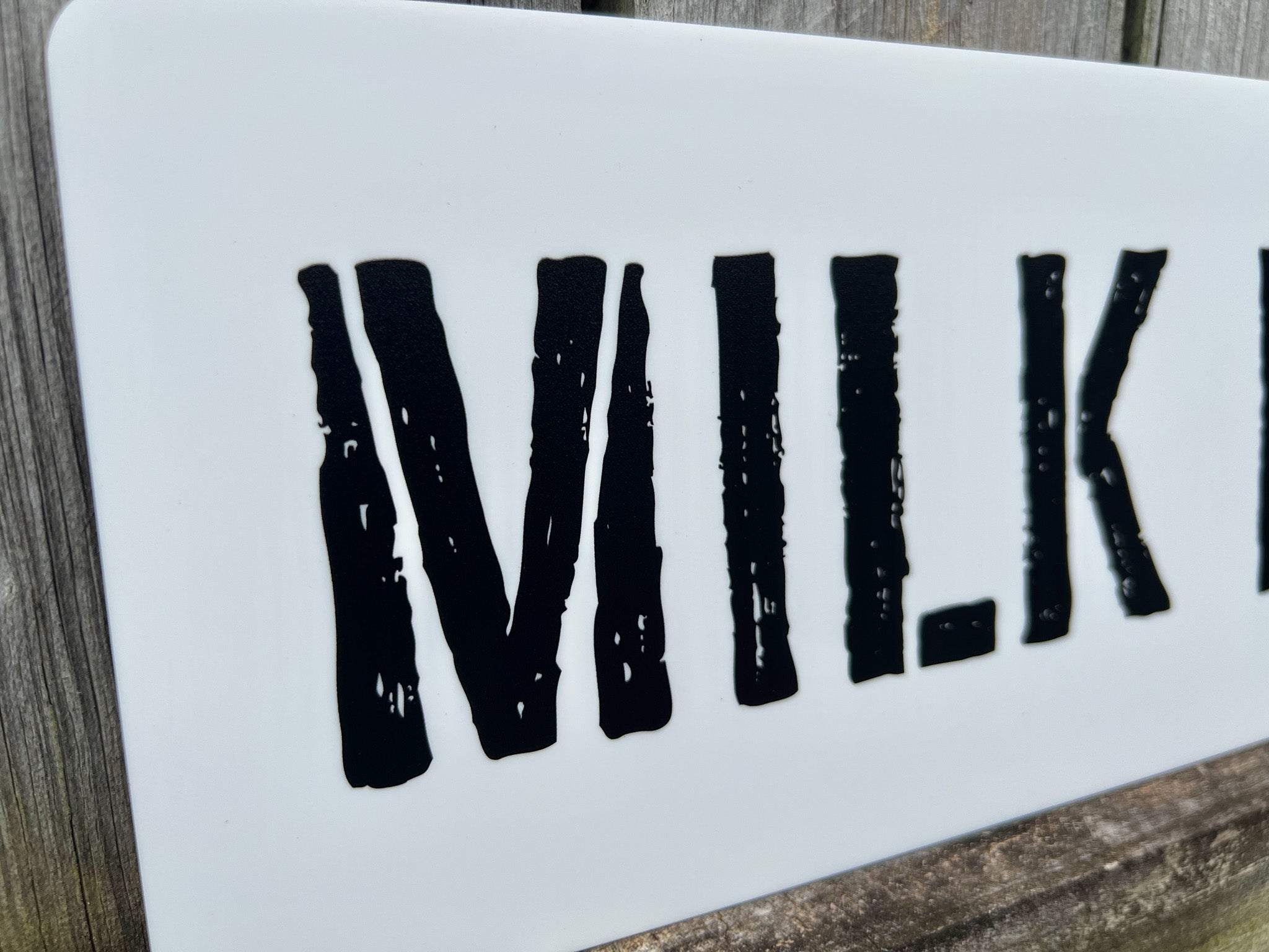 A personalised sign that reads 'MILK' in a distressed stencil style font.