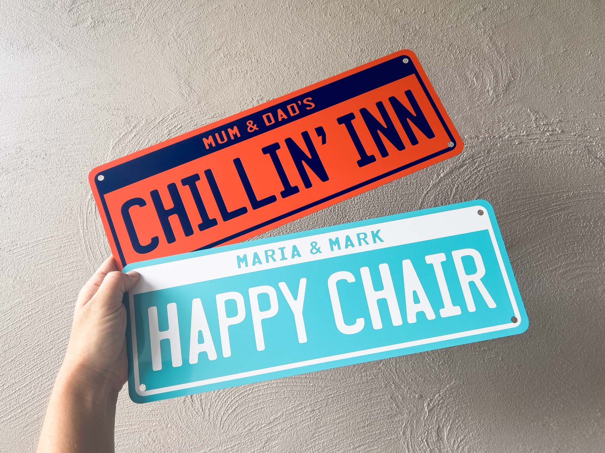 Two decorative number plates signs with personalised text held against a light grey background