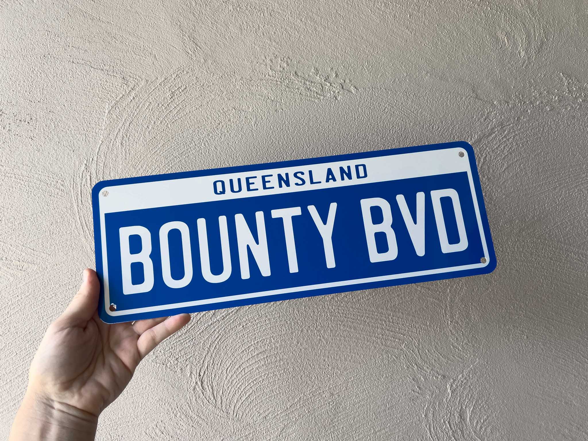 Hand holding a blue and white plate with 'Queensland Bounty BVD' text against a beige wall.