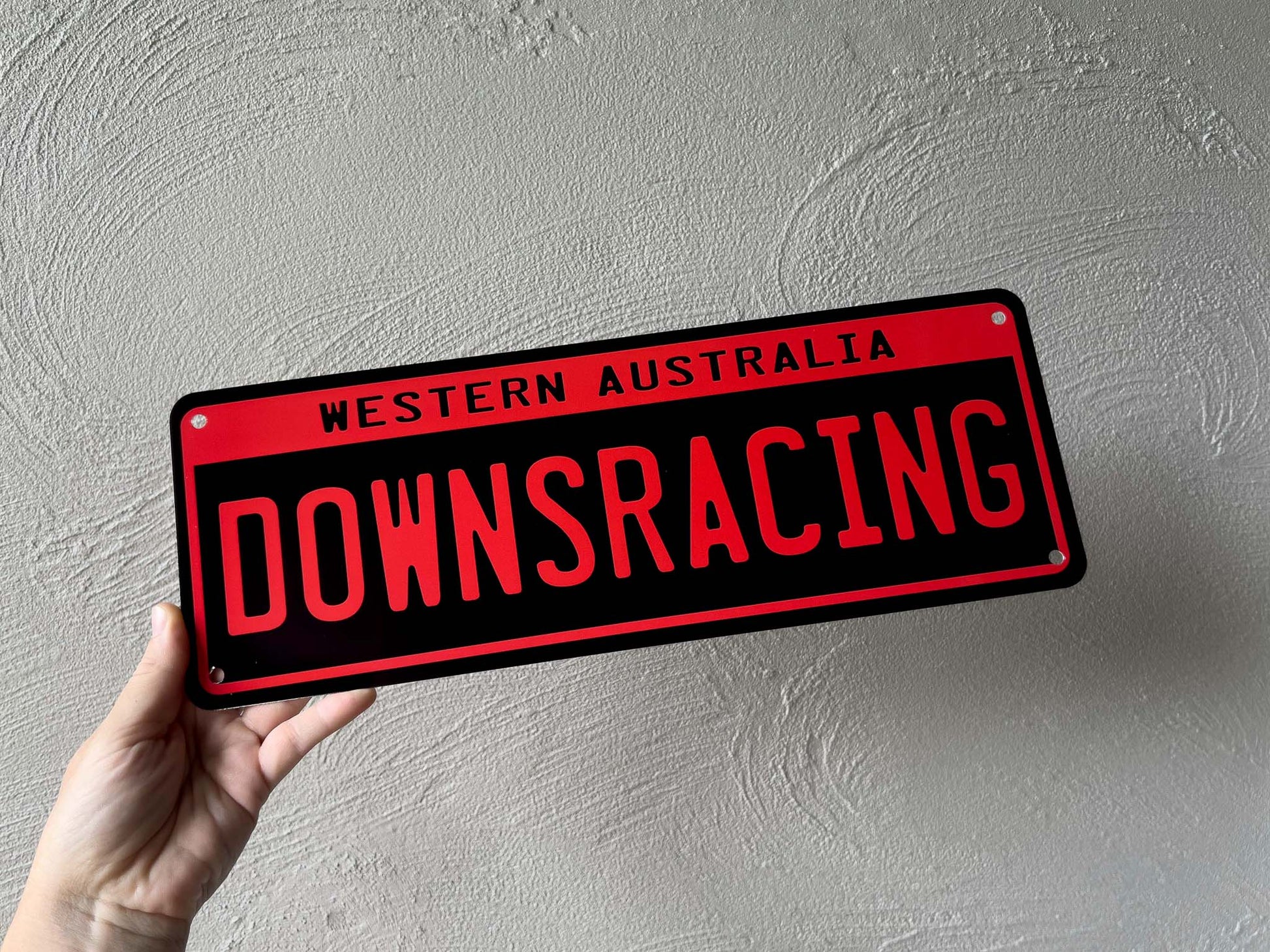 Hand holding a red and black sign with 'Western Australia Downs Racing' text against a gray background