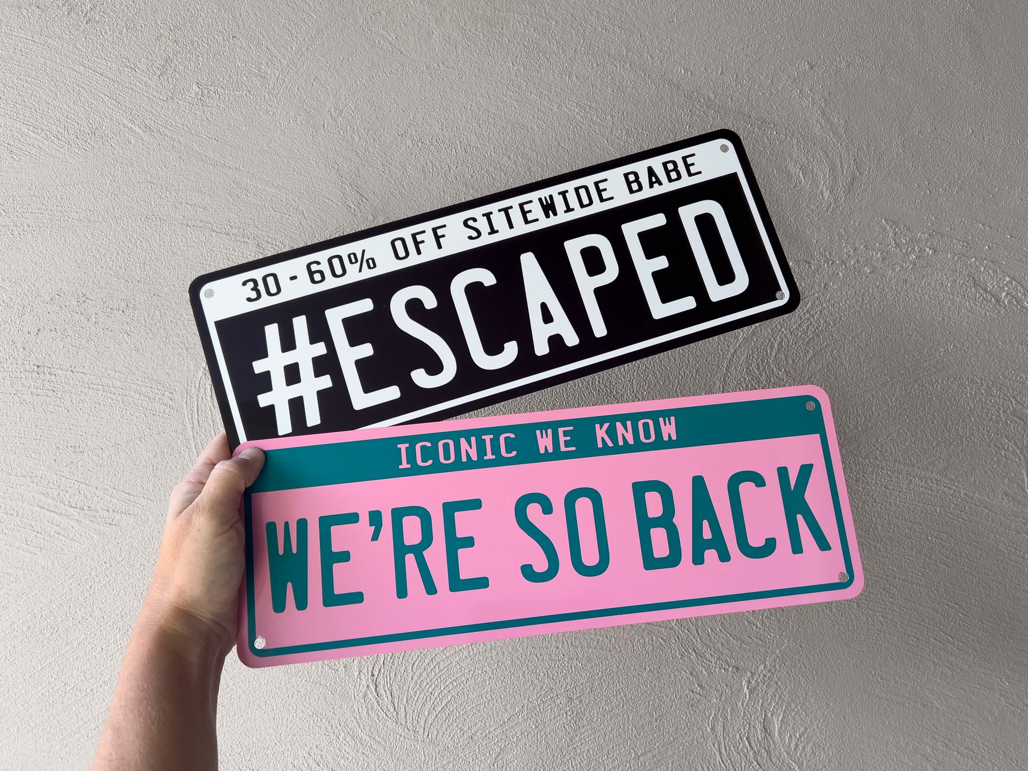 Two business signs in the shape and style of a license plate in black and pink 