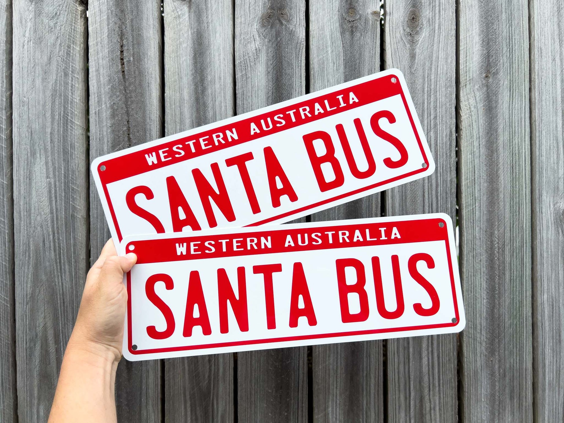 Two red and white 'Santa Bus' signs held against a wooden fence.