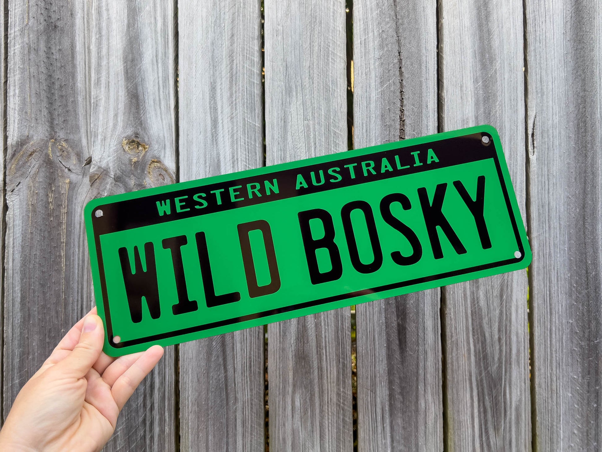 Green novelty number plate with 'WILD BOSKY' text held against a wooden fence background