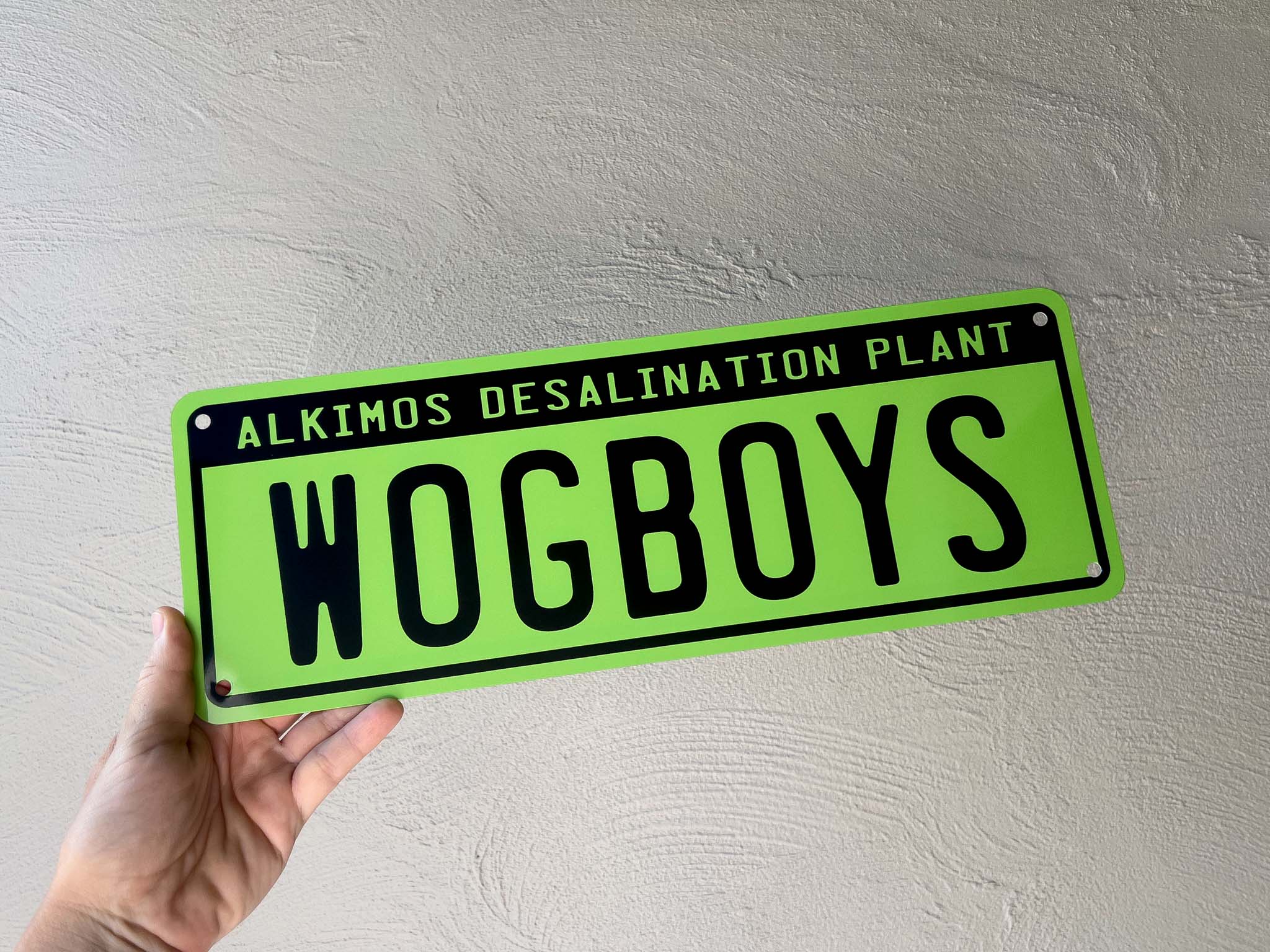 Hand holding a green sign with black text against a light gray background
