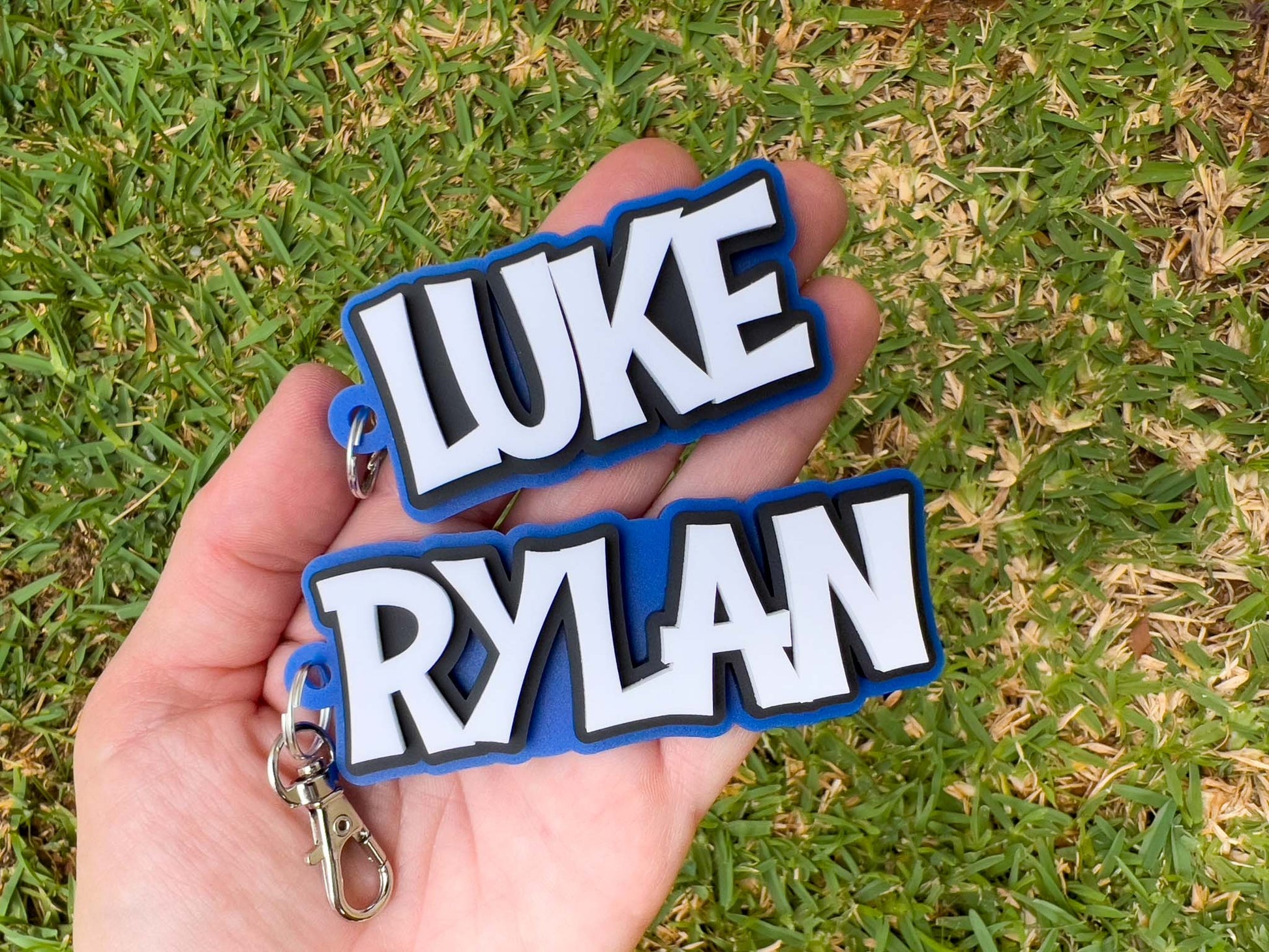 Two custom 3D acrylic keychains in blue, black and white that say 'LUKE' & 'RYLAN'.