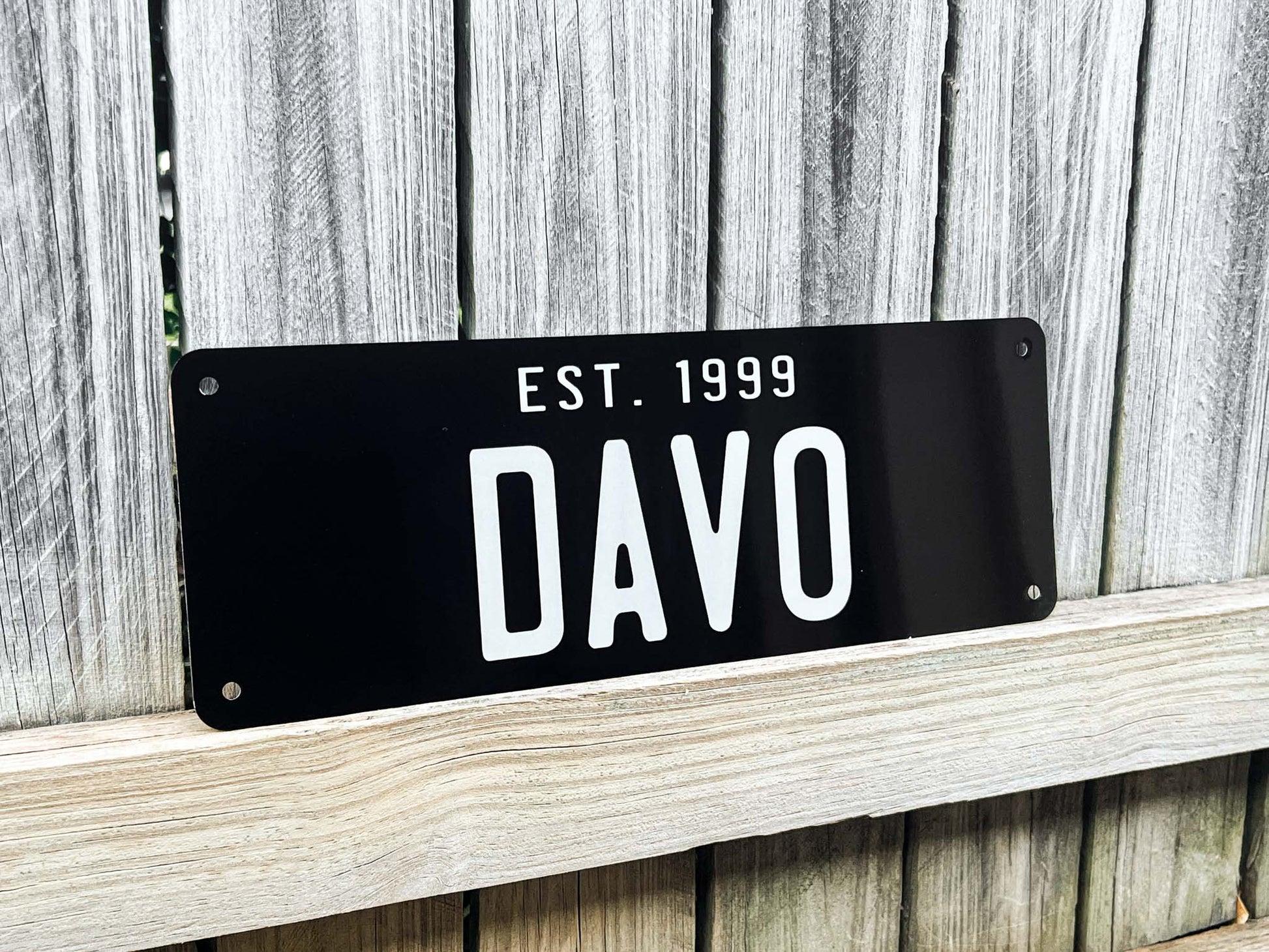 Black sign with 'DAVO' and 'EST. 1999' text on a wooden background