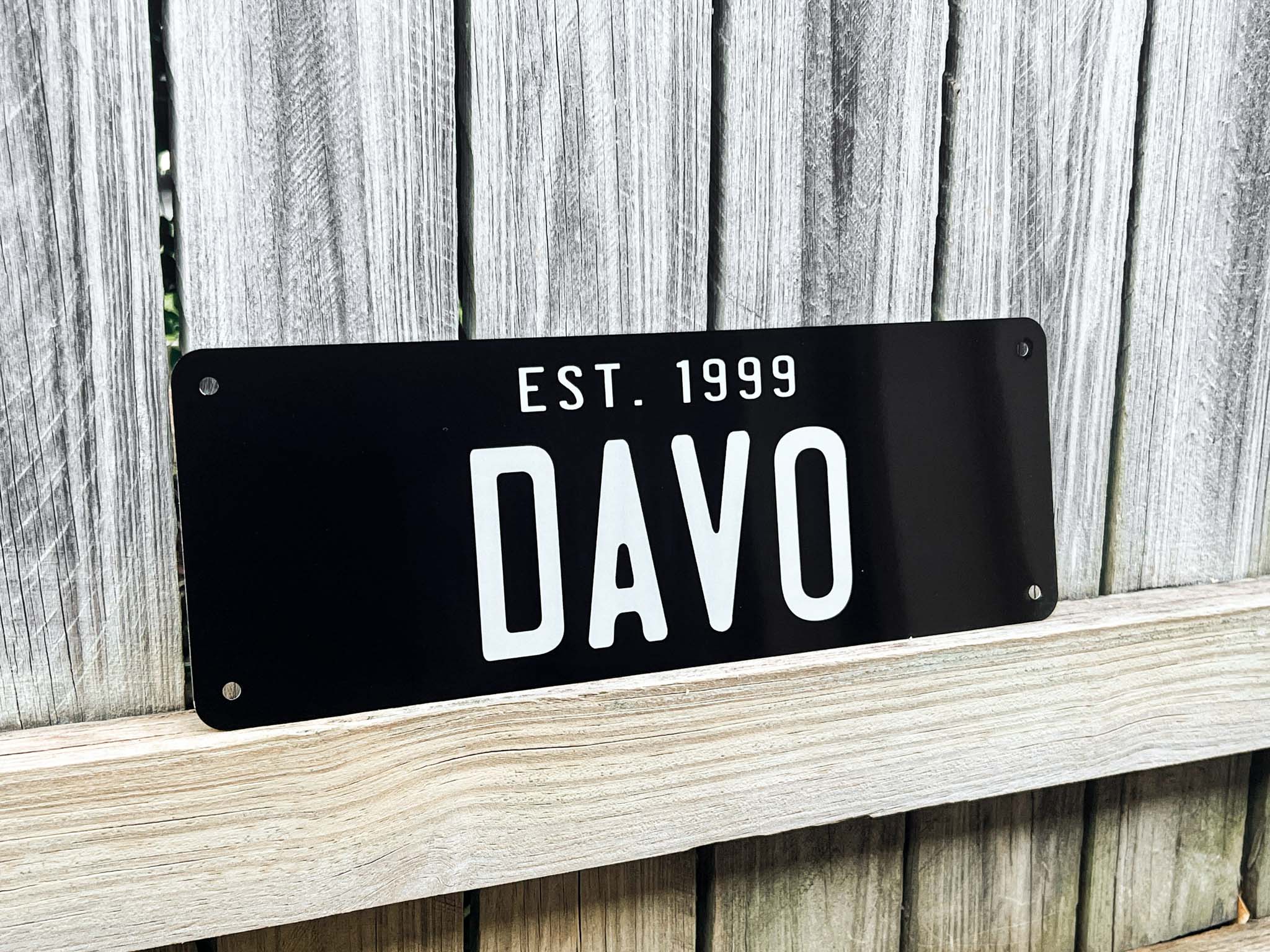 Black sign with 'DAVO' and 'EST. 1999' text on a wooden background