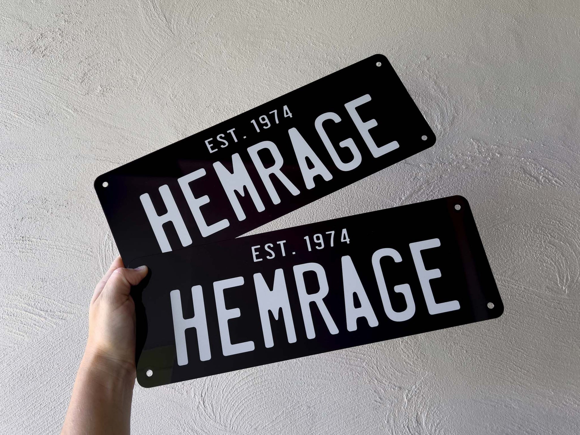 Two black metal signs with 'HEMRAGE' and 'EST. 1974' text on a light gray background.