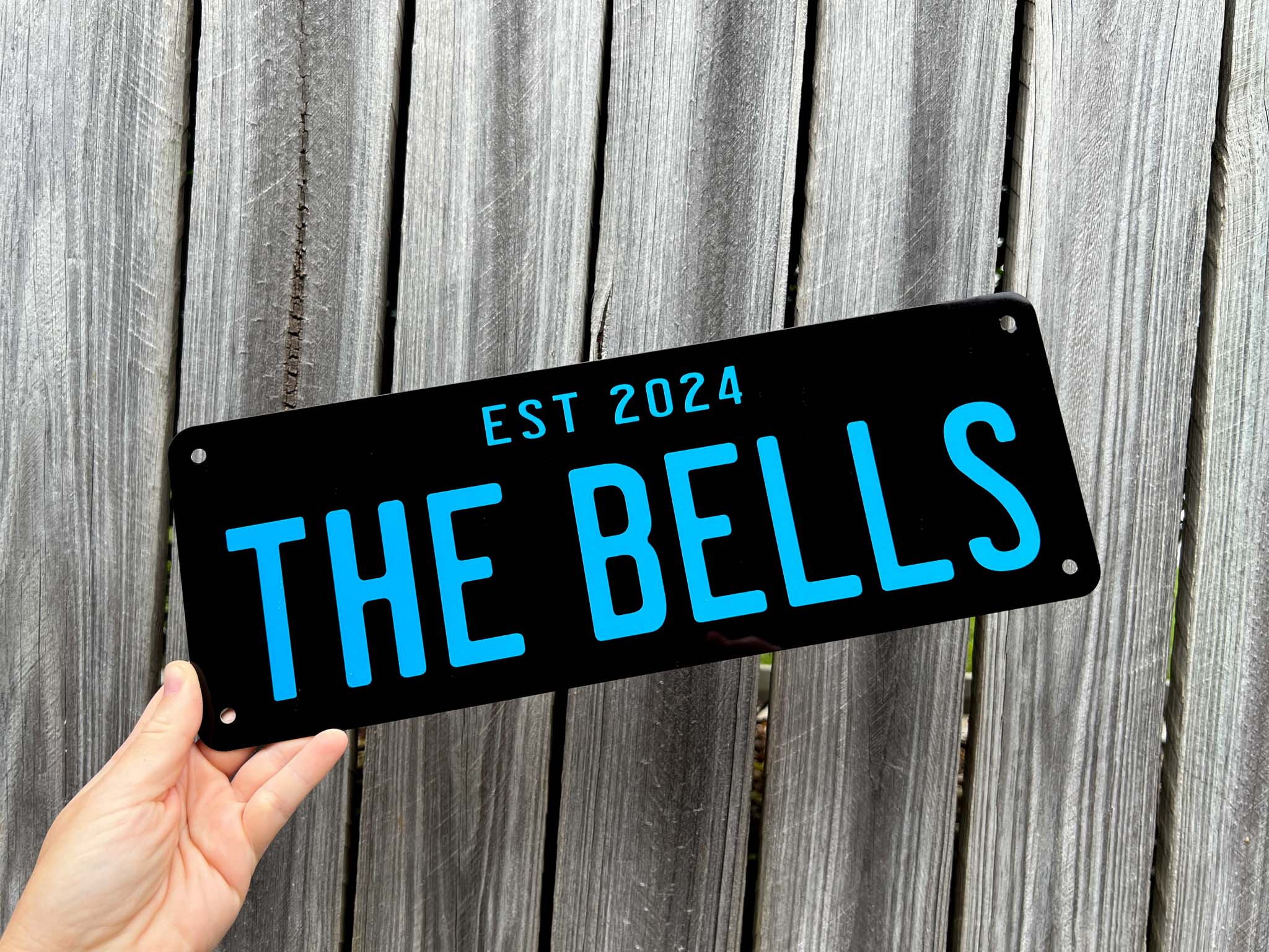 Hand holding a plate with 'THE BELLS EST 2024' in blue and black