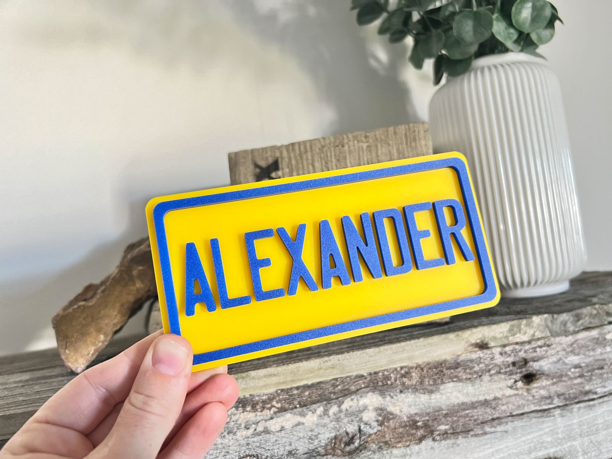 A yellow laser cut acrylic mini name plaque with 'Alexander' cut in blue 3D letters