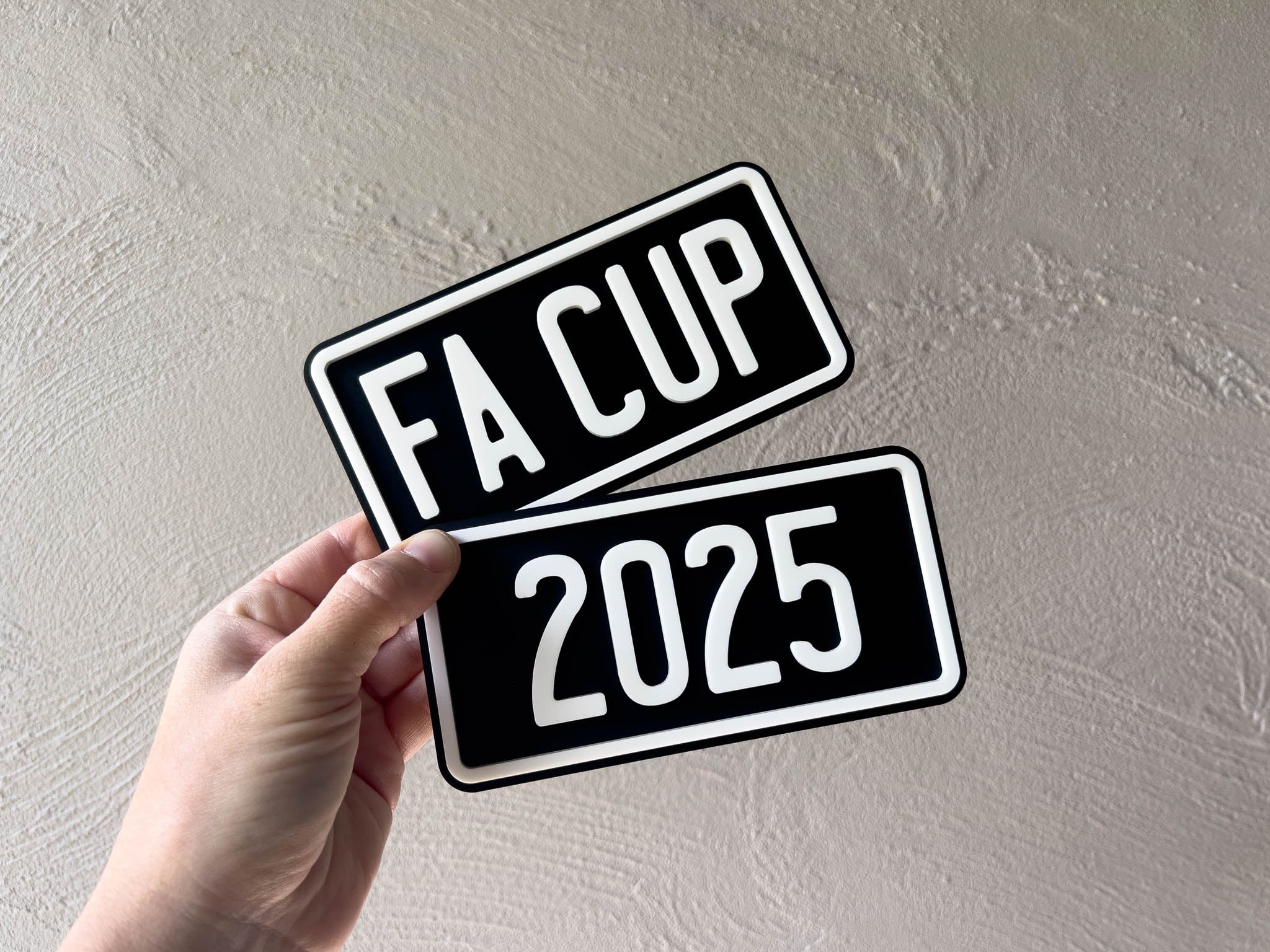 Hand holding two FA Cup 2025 custom acrylic plates against a plain background