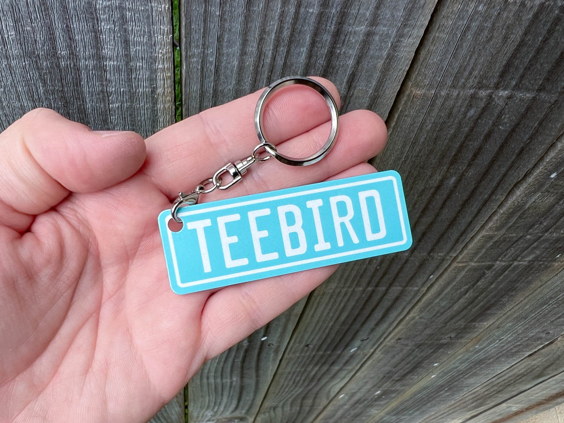 Hand holding a blue keychain with 'TEEBIRD' text against a wooden background