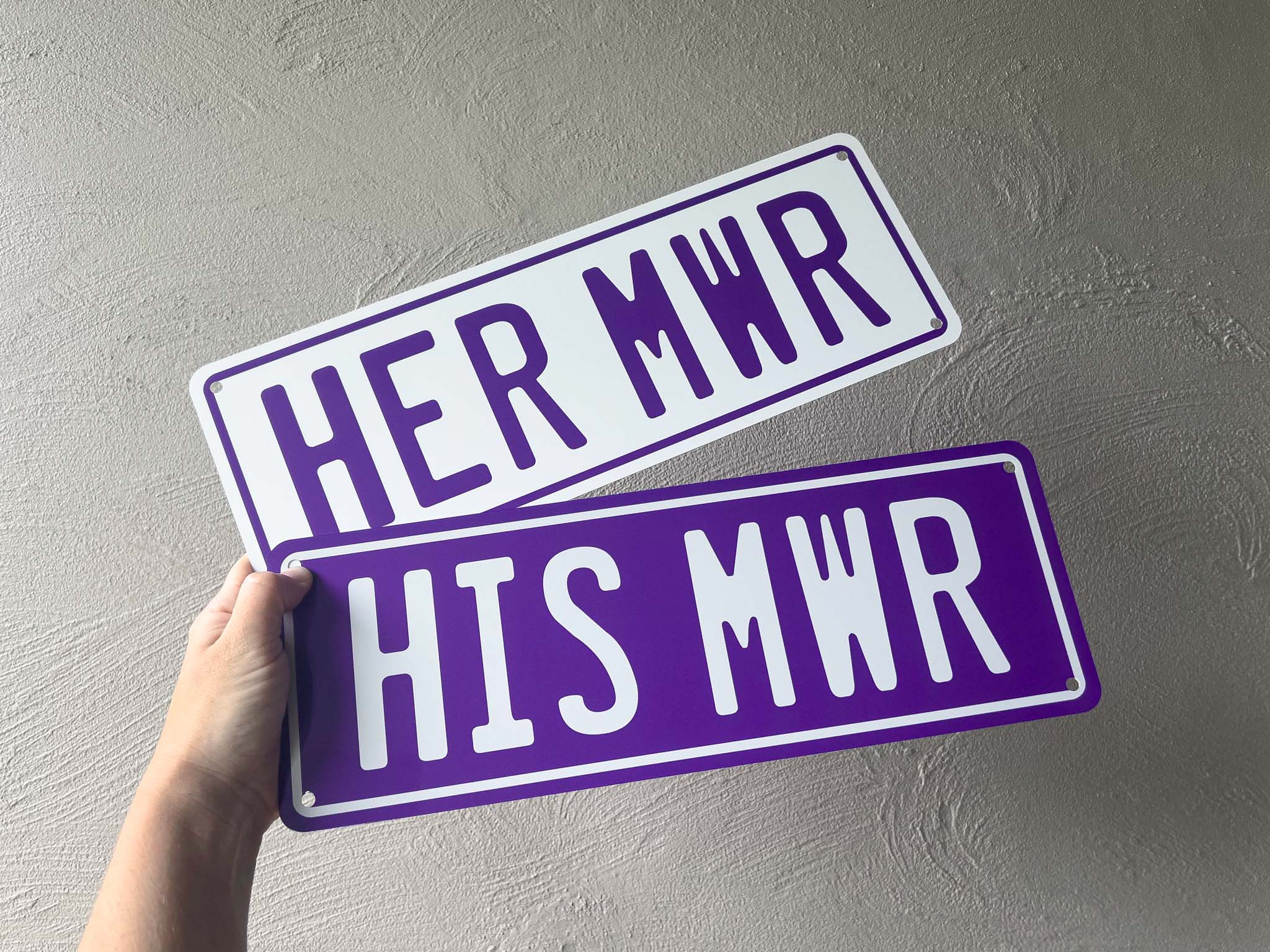 Two purple metal plates with 'HER MWR' and 'HIS MWR' text held against a grey background.