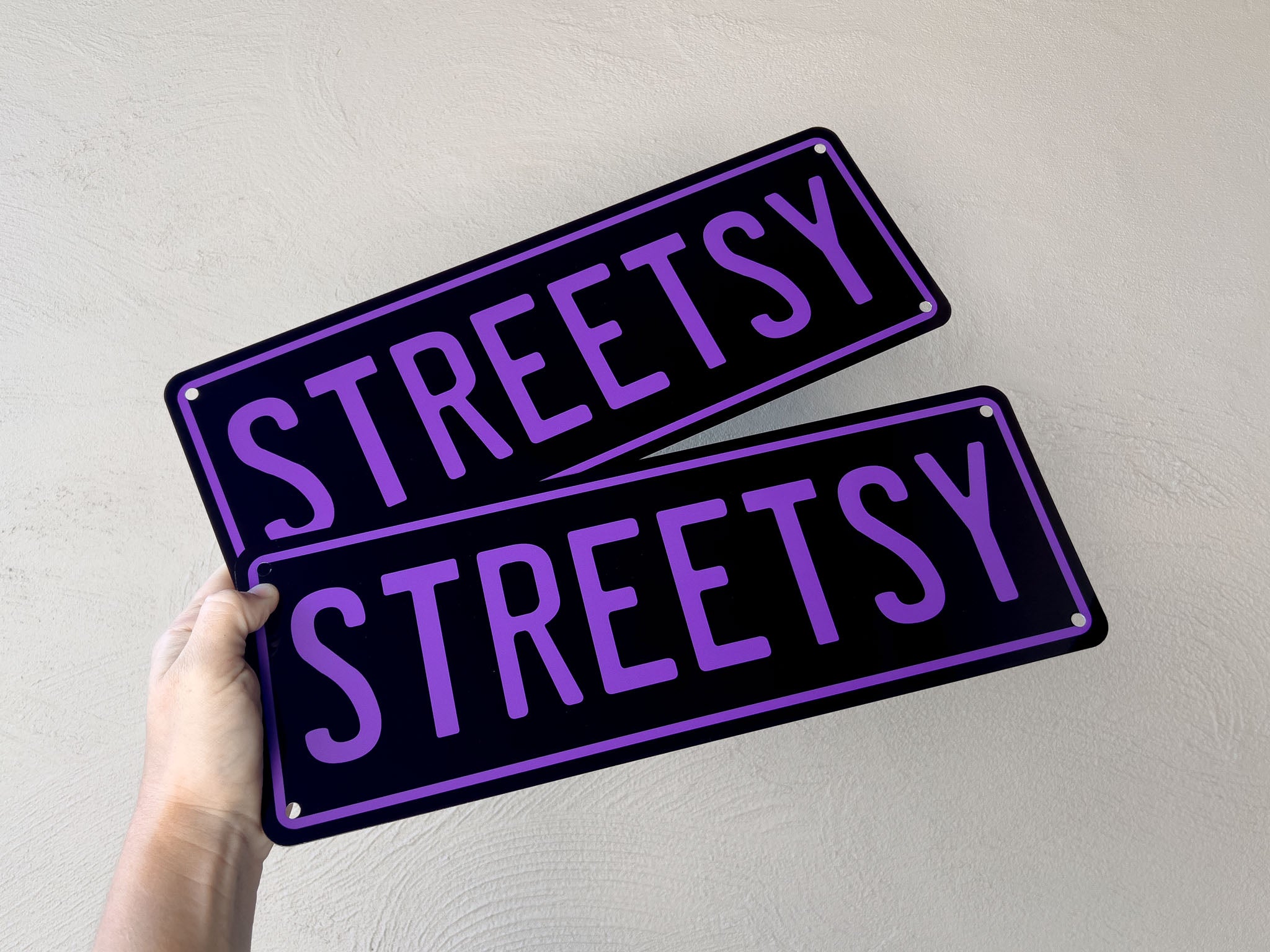 Two custom printed black and purple 'STREETSY' signs held against a light grey background