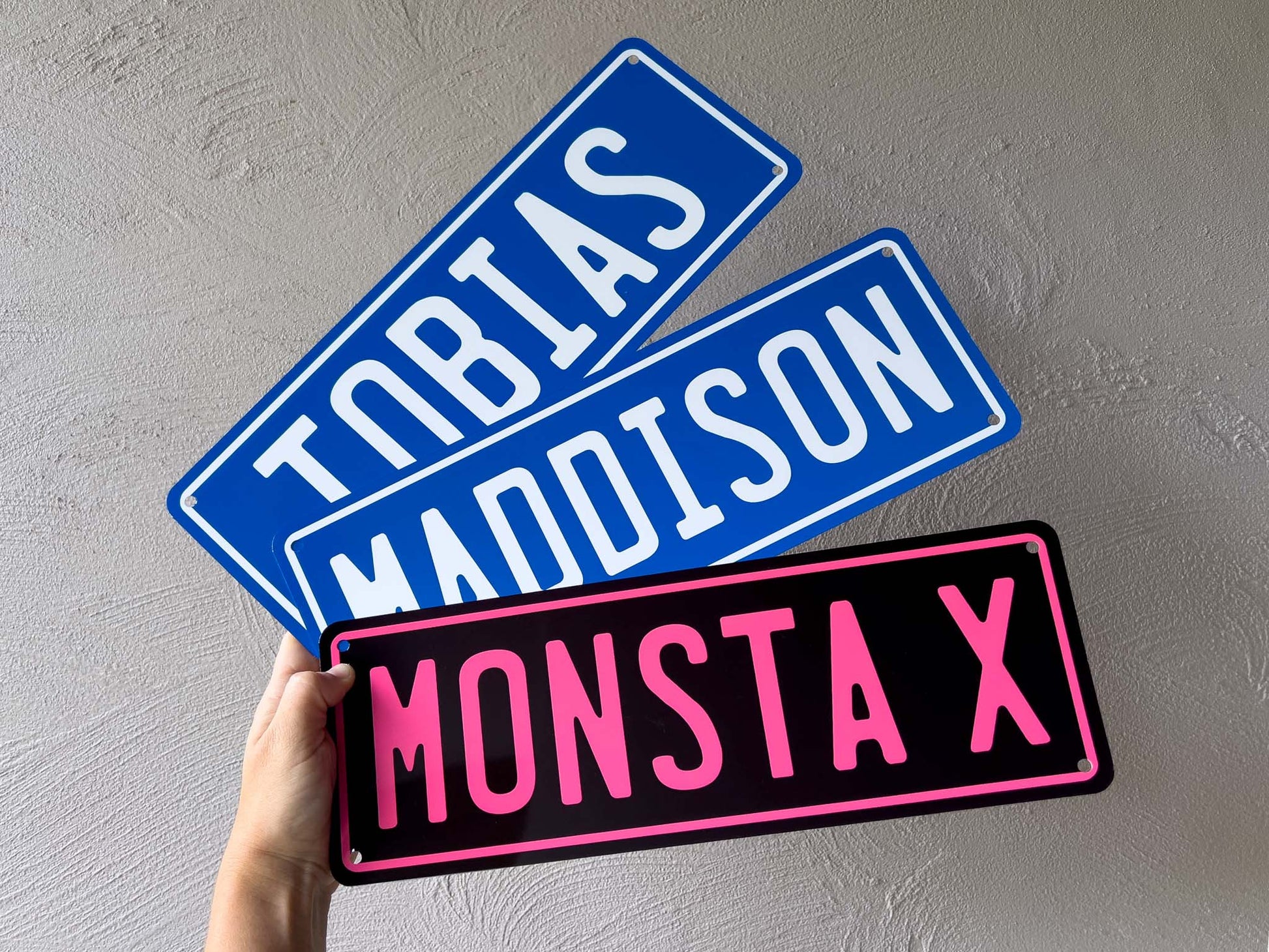 Three colorful name plates held against a gray wall.
