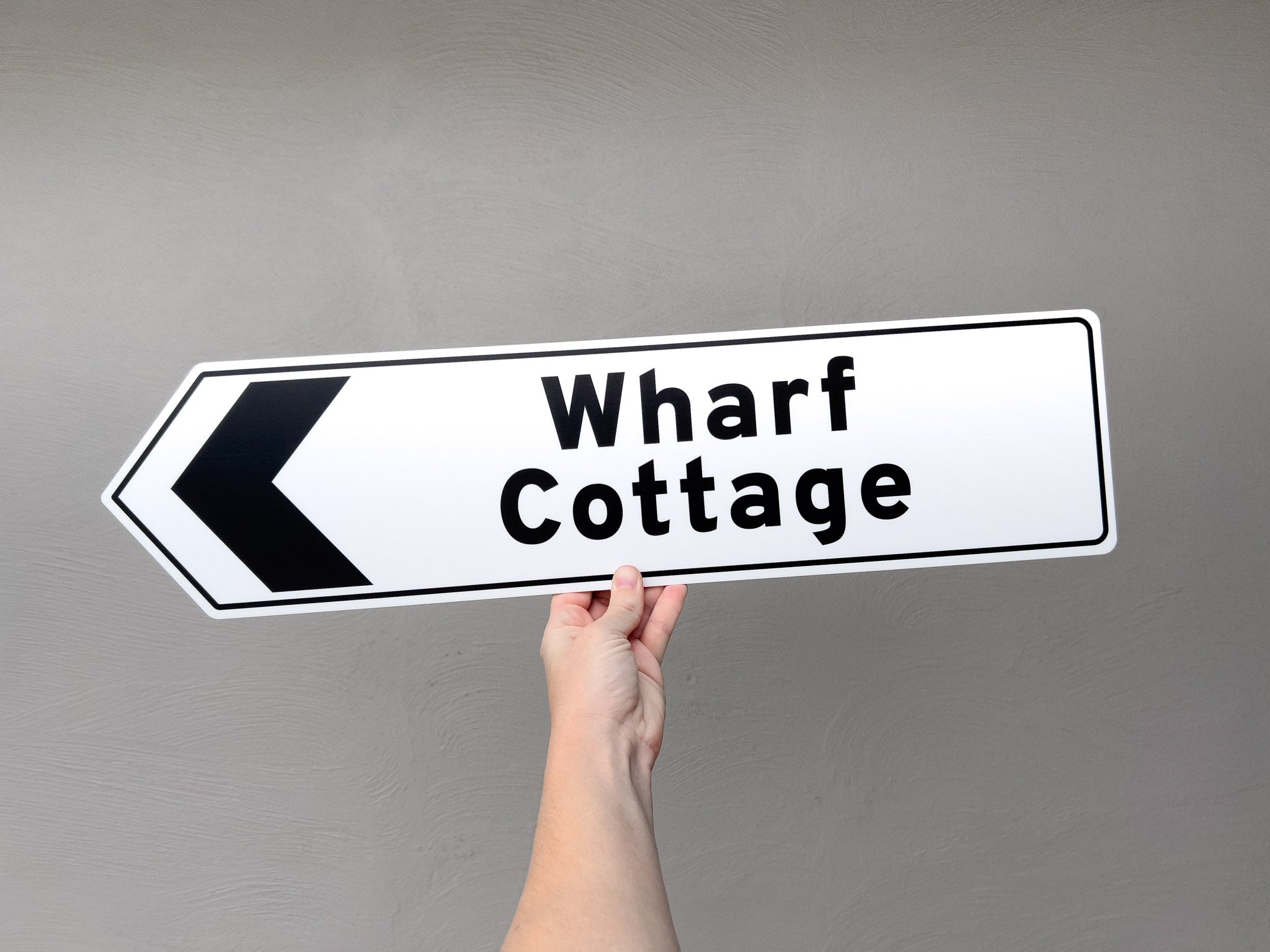 A fun novelty direction sign that reads 'Wharf Cottage' in white and black.