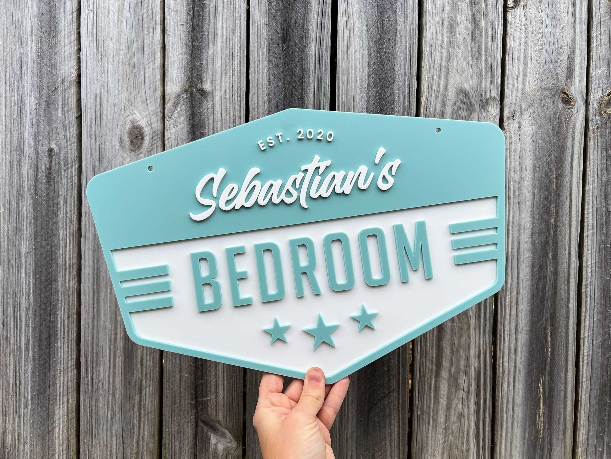 Hexagonal sign in a seaside blue colour with 'Sebastian's Bedroom' text against a wooden background