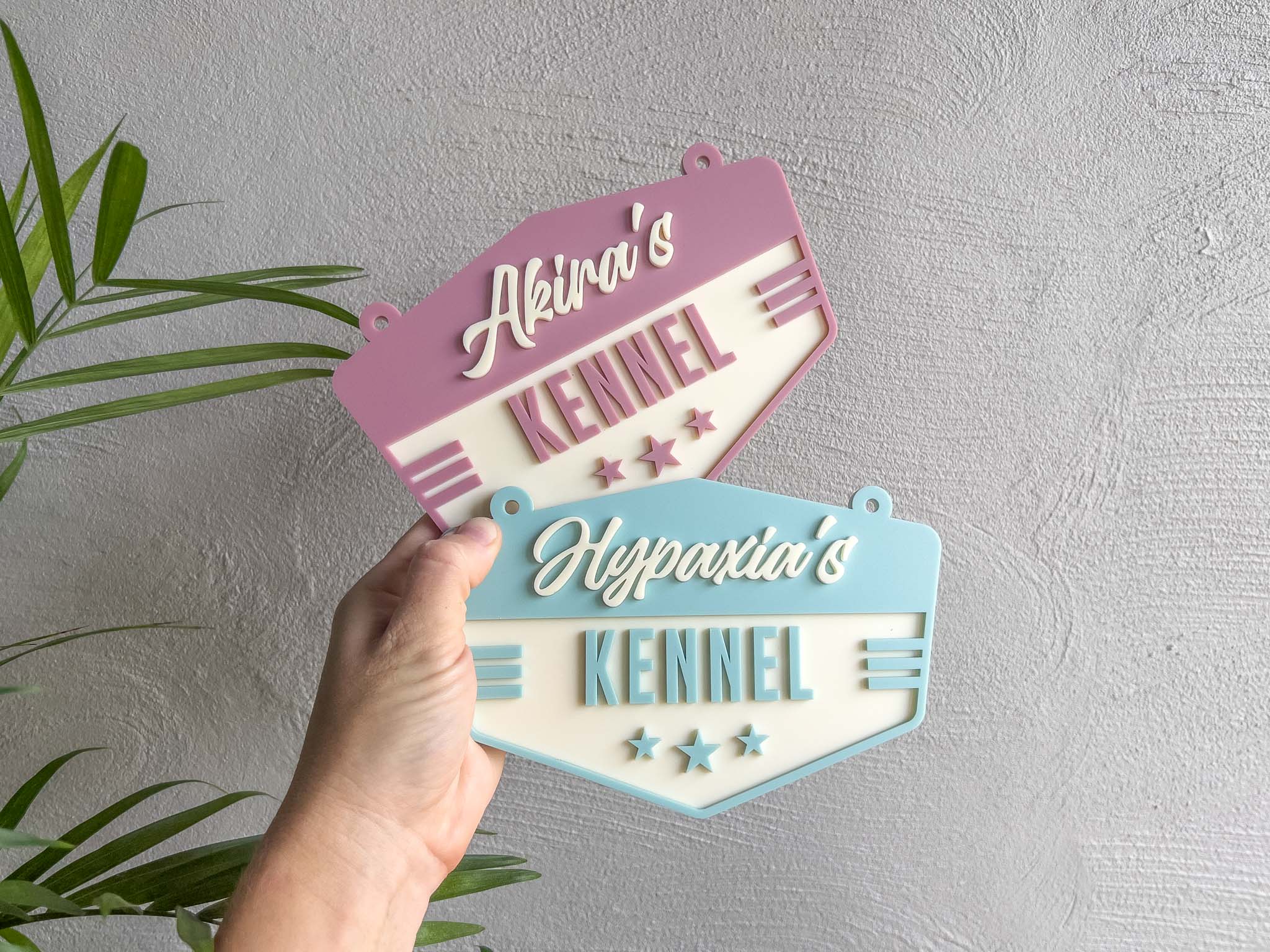 Hand holding two decorative signs with 'Akira's Kennel' and 'Hypaxia's Kennel' text against a grey background | Coji Designs