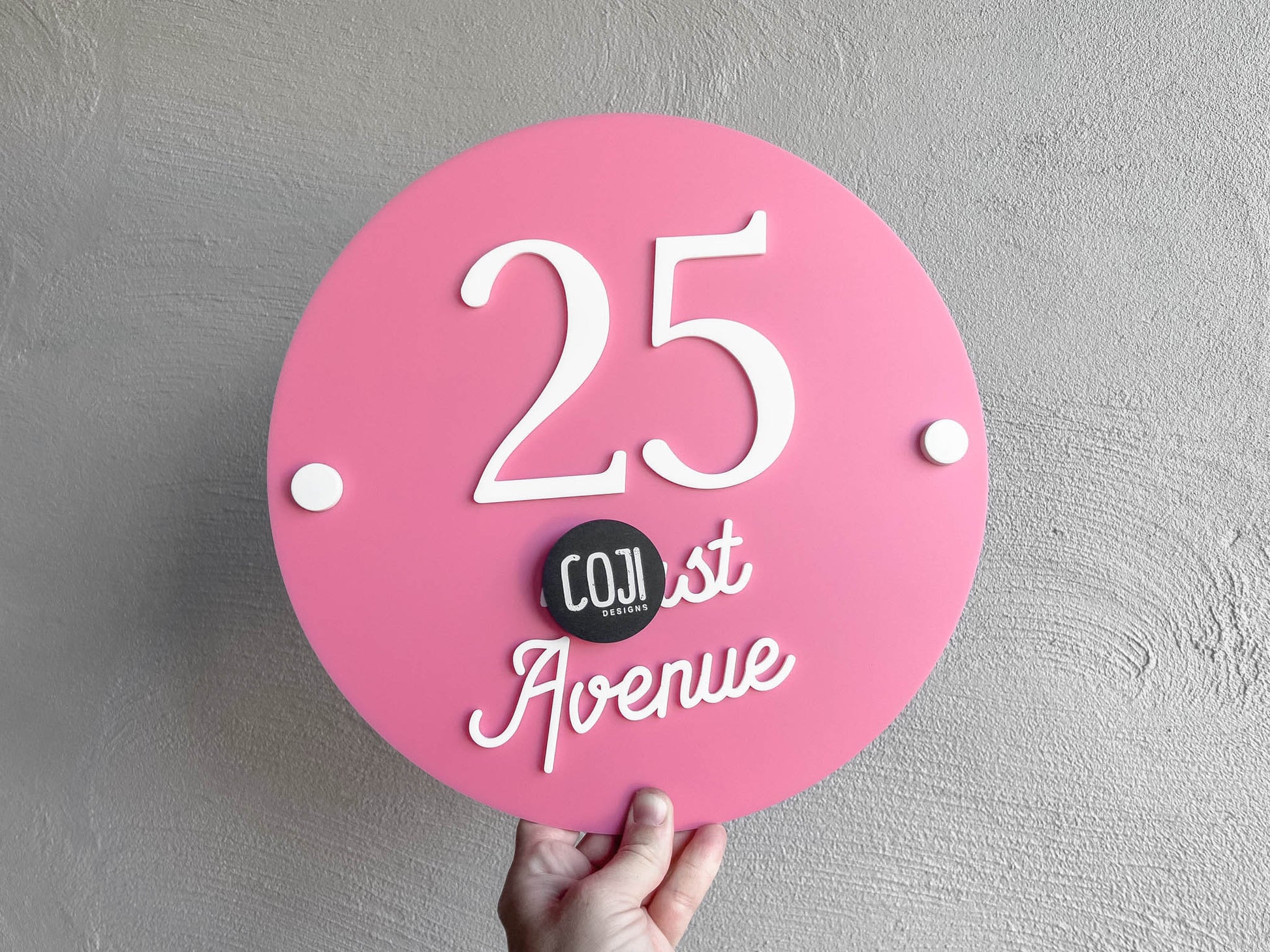Cotton candy pink round address plaque with white text that says '25 Avenue'.