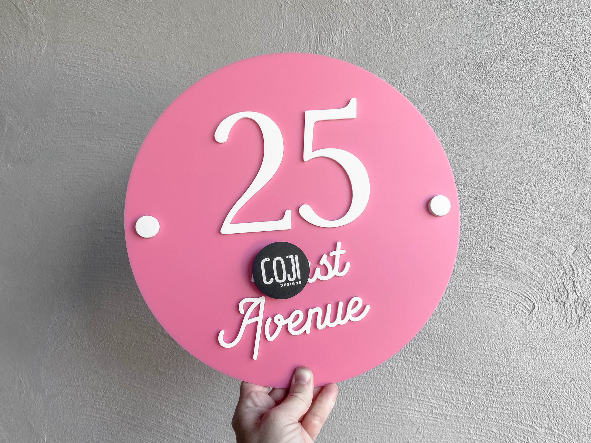 Cotton candy pink round address plaque with white text that says '25 Avenue'.