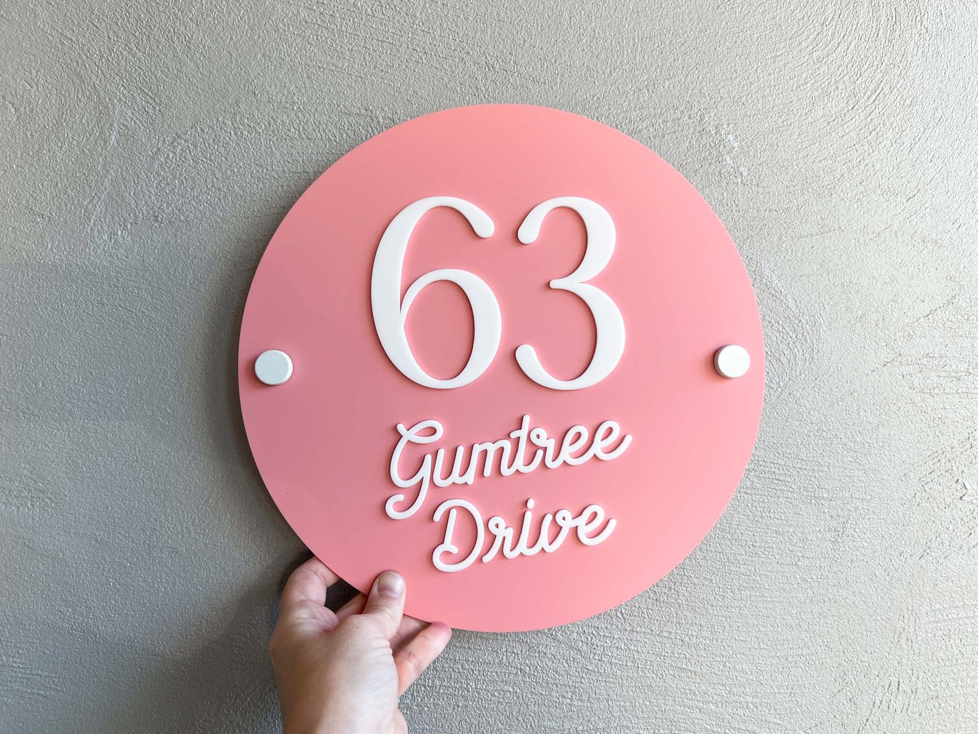 Personalised round 3D acrylic melon pink house number plaque that says '63 Gumtree Drive'.