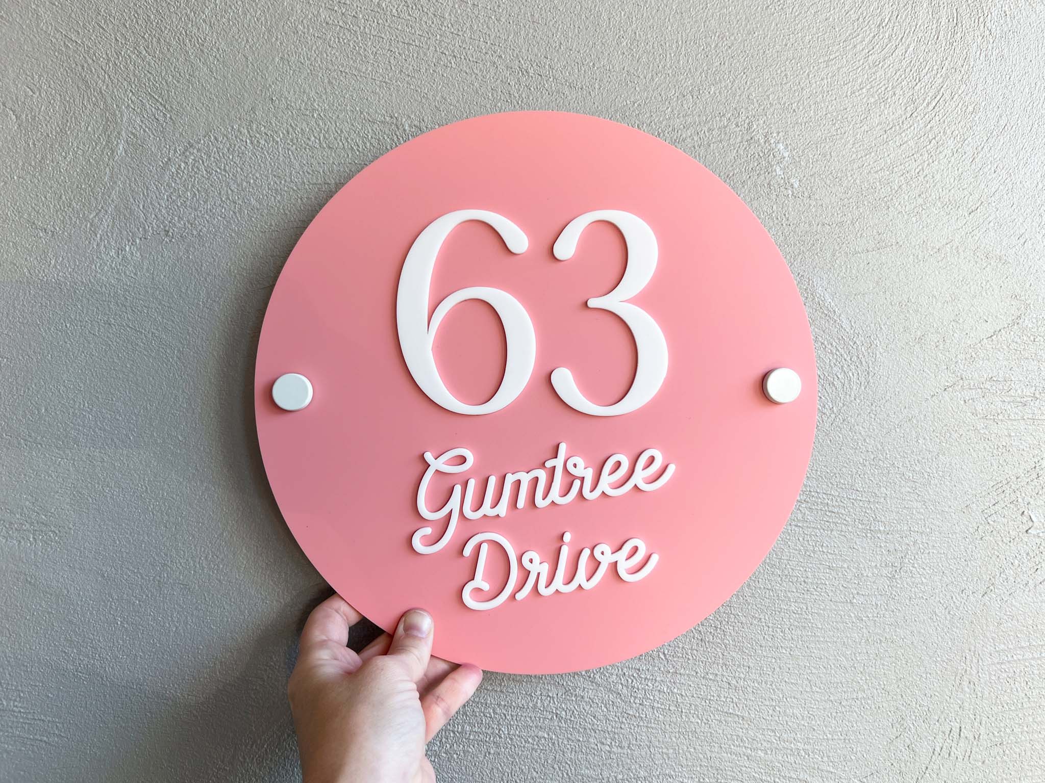 Personalised round 3D acrylic melon pink house number plaque that says '63 Gumtree Drive'.