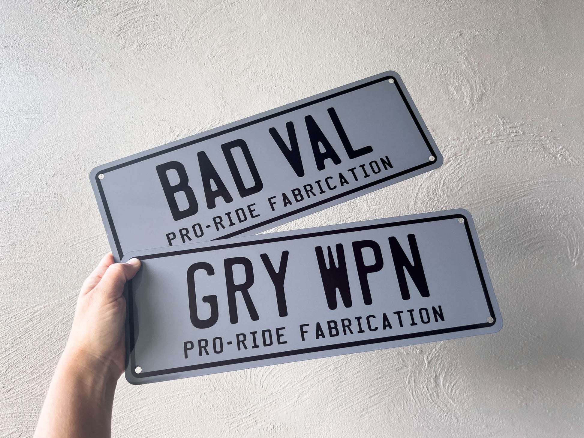 Two metal signs with text held by a hand against a light gray background