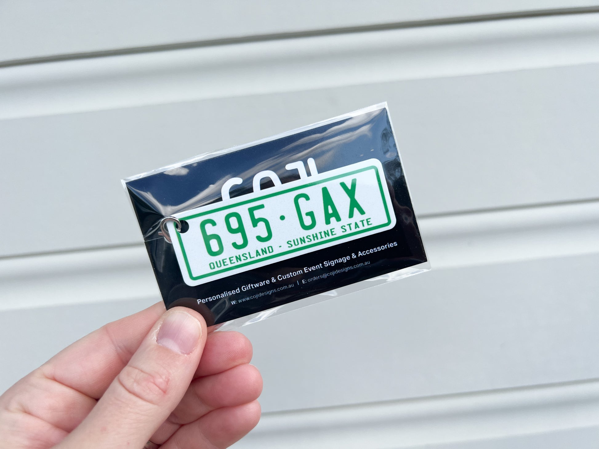 Hand holding a green license plate keychain with text against a metal background