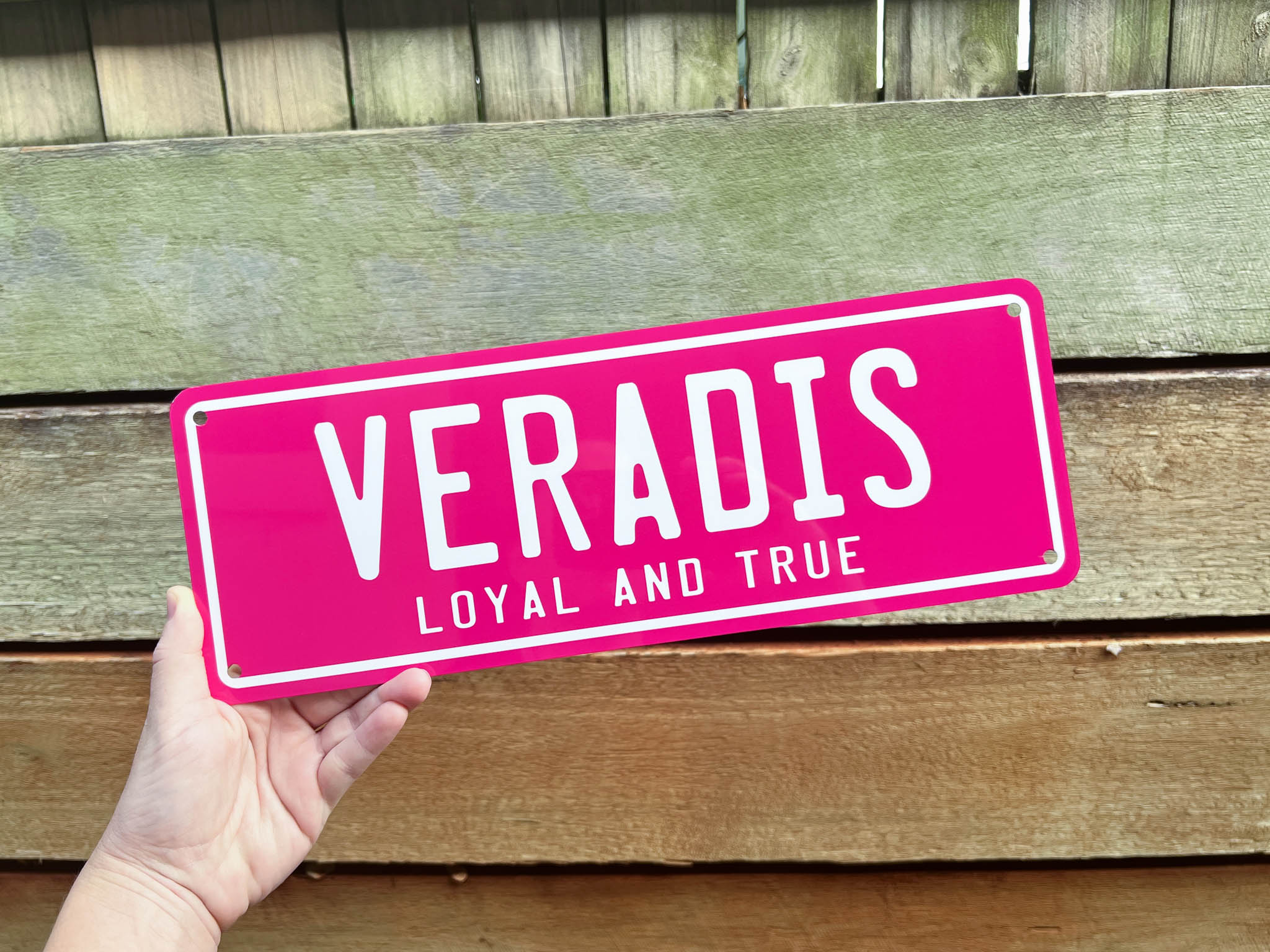Pink sign with 'VERADIS LOYAL AND TRUE' text held by a hand against a wooden background