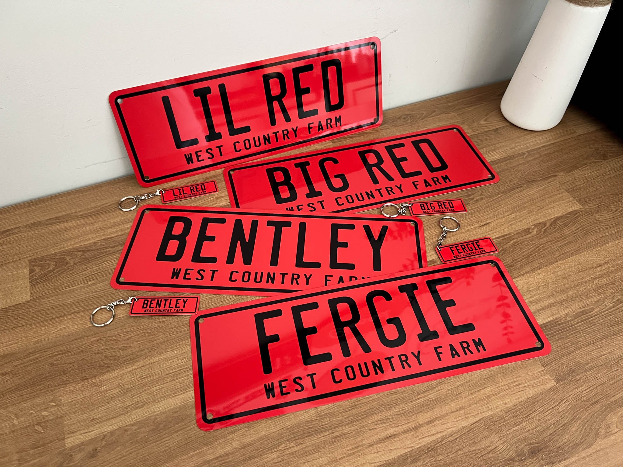 Collection of novelty plates and matching keychains the say various names for 'West Country Farm' in red and black.