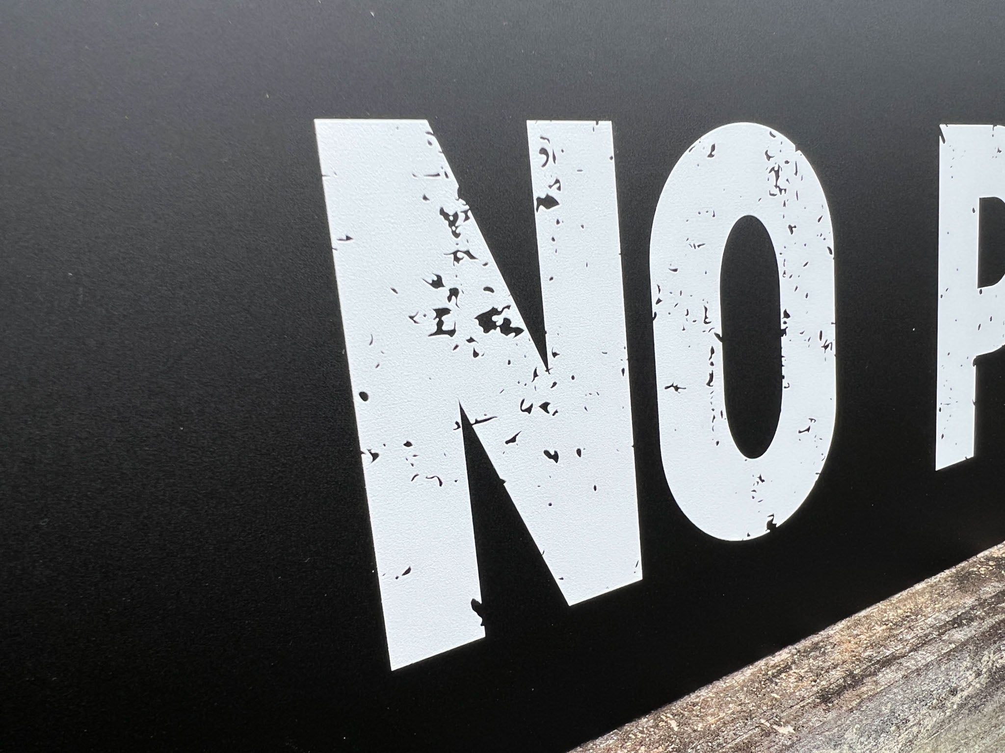 Close-up of a 'No Parking' sign with white textured text on a black background.