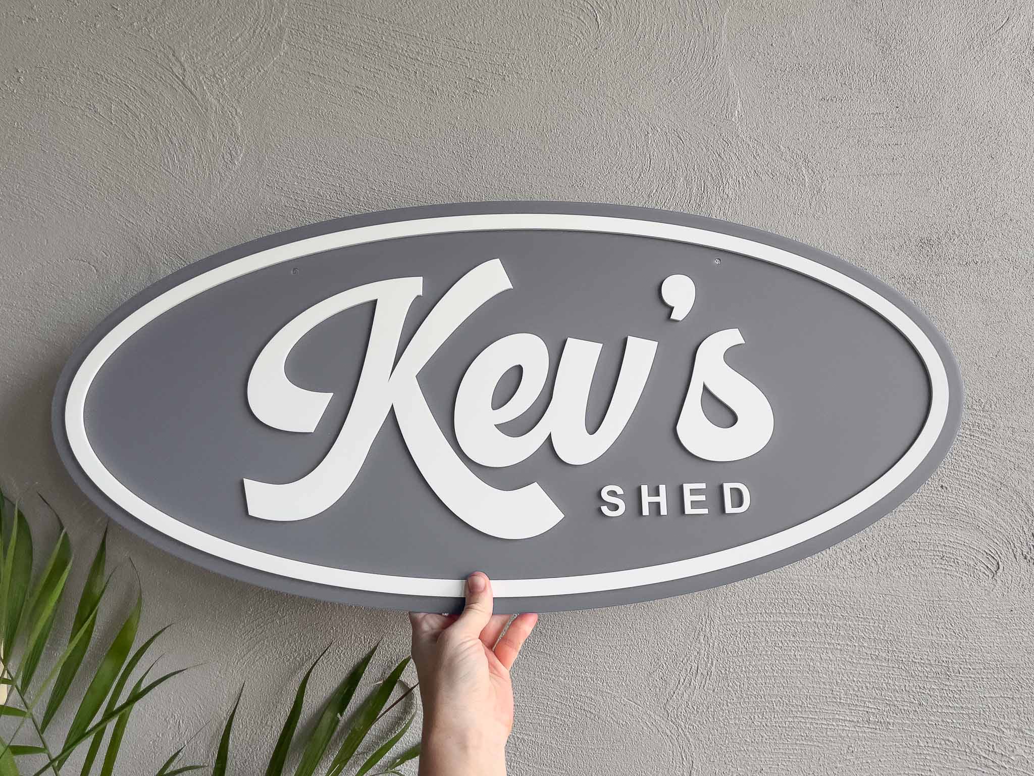 Oval custom made 3D acrylic sign with 'Kev's Shed' in grey and white.