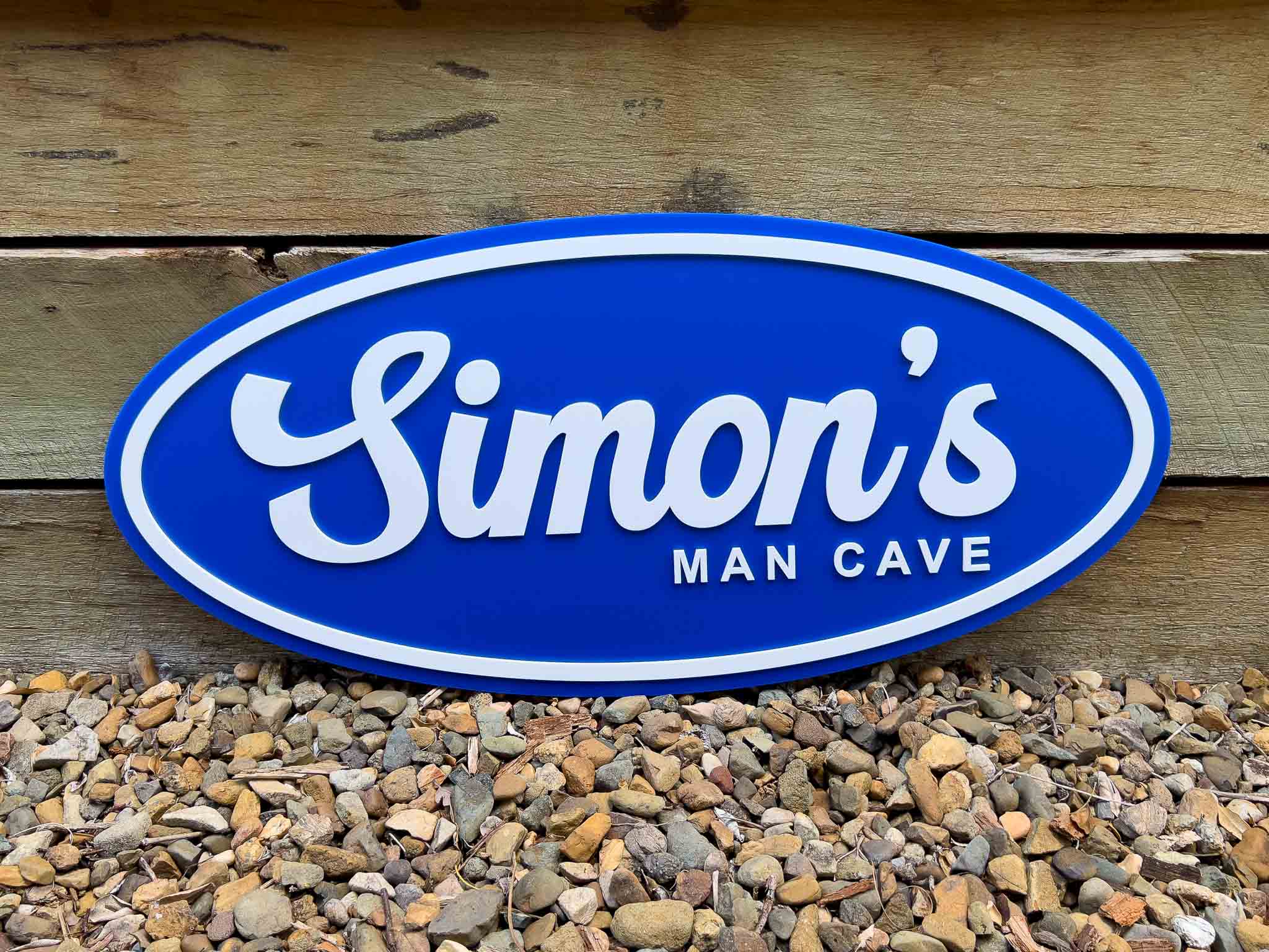 Blue oval badge sign with 'Simon's Man Cave' text on a wooden background