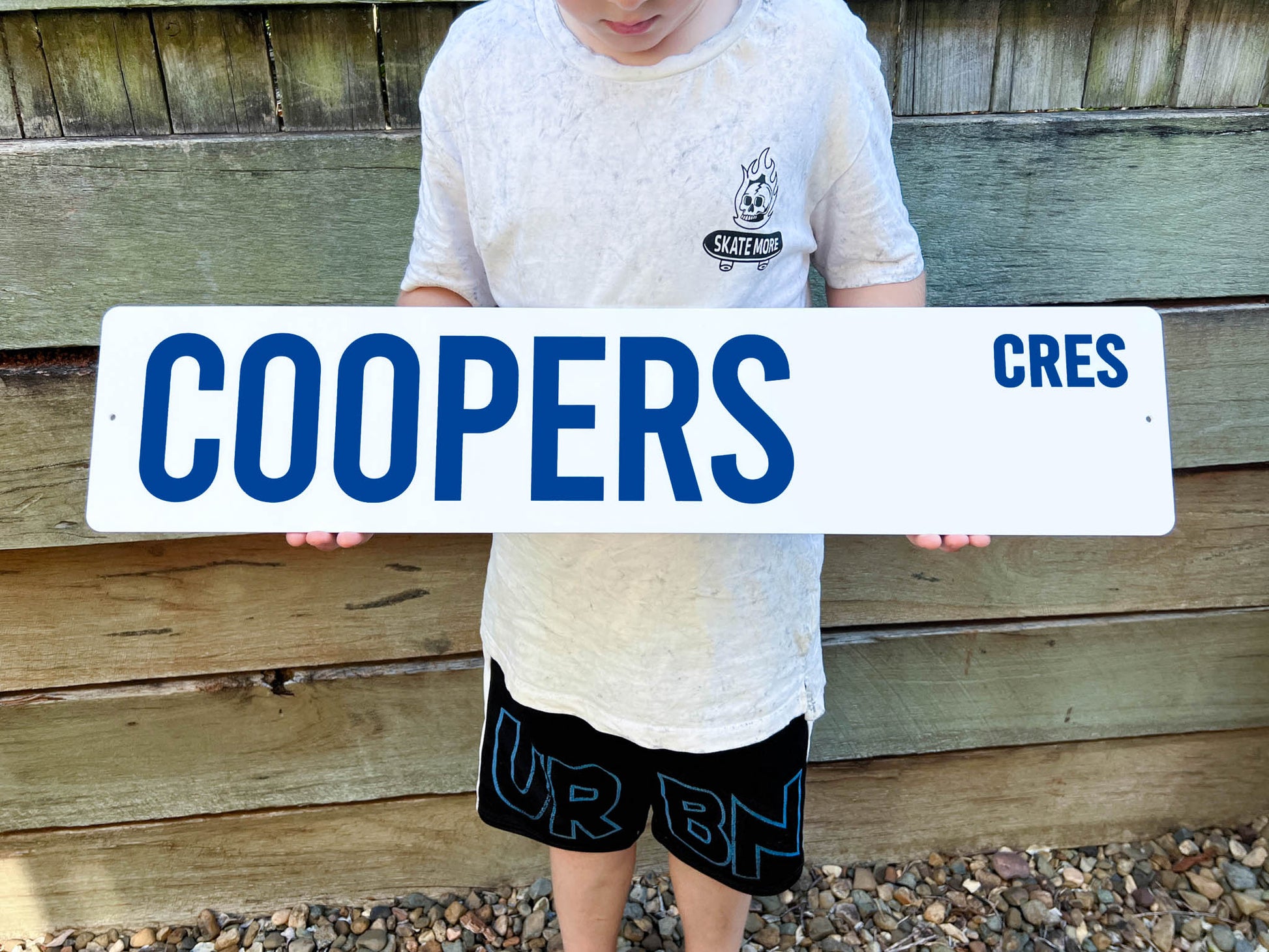 Person holding a street sign with 'Coopers Cres' against a wooden fence background
