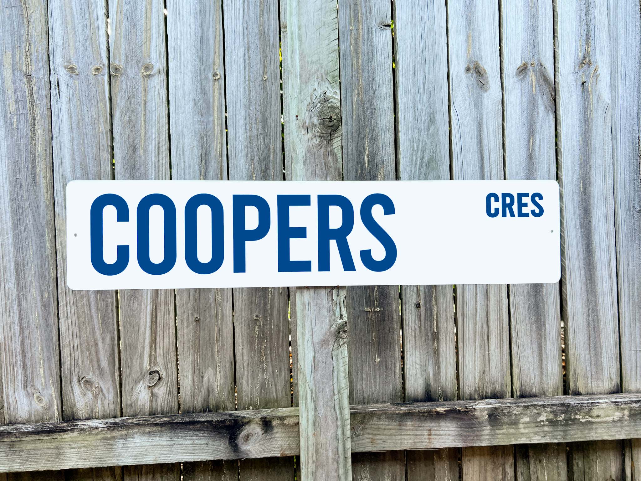 Street sign with 'COOPERS CRES' text against a wooden fence background