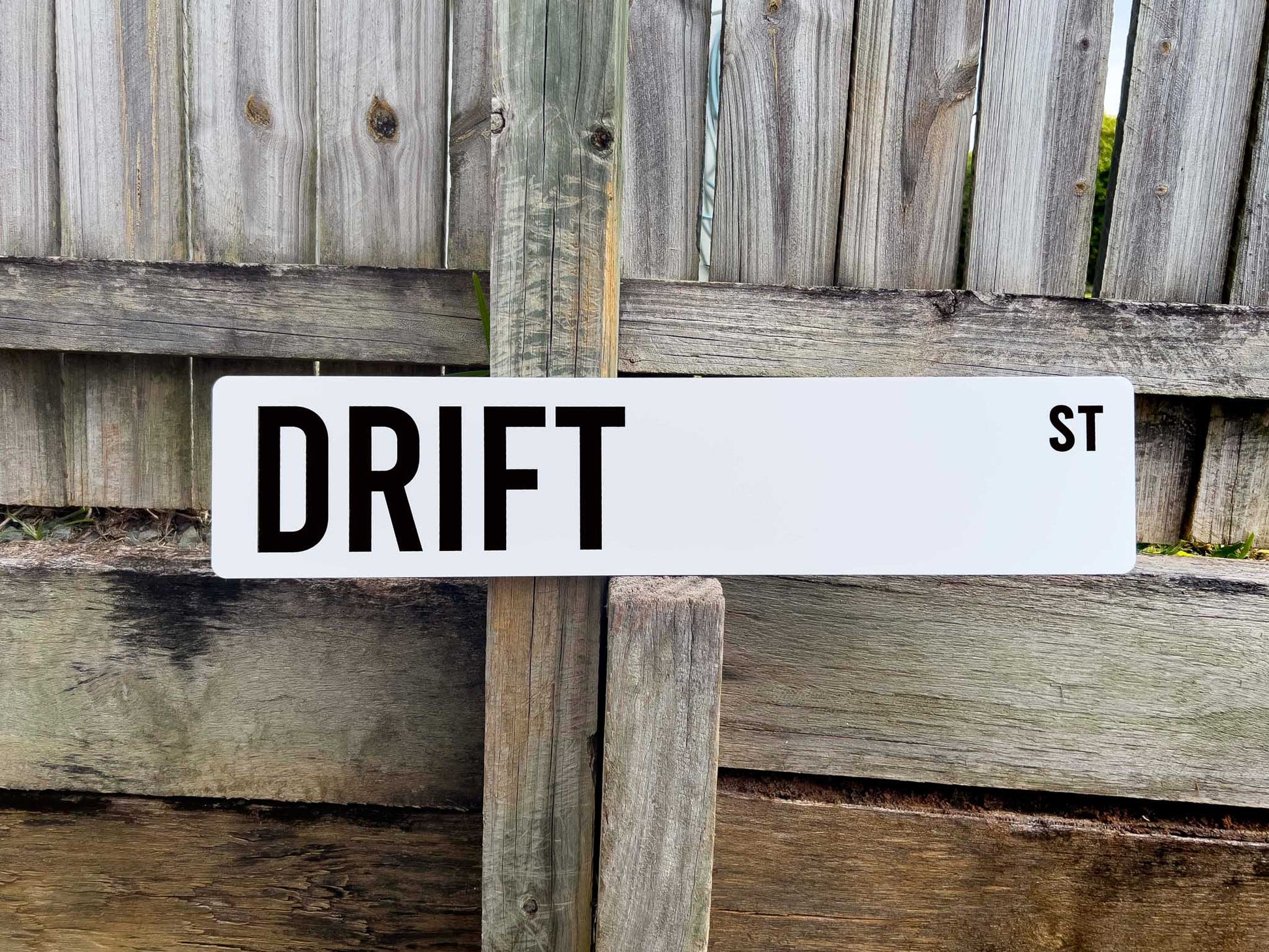 White and black street sign reading 'DRIFT ST' against a wooden fence background