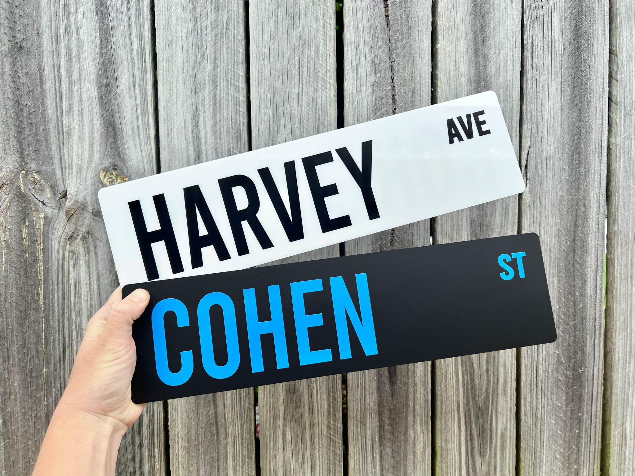 Two nostalgic street signs, one labeled 'Harvey Ave' and the other 'Cohen St', held against a wooden background.