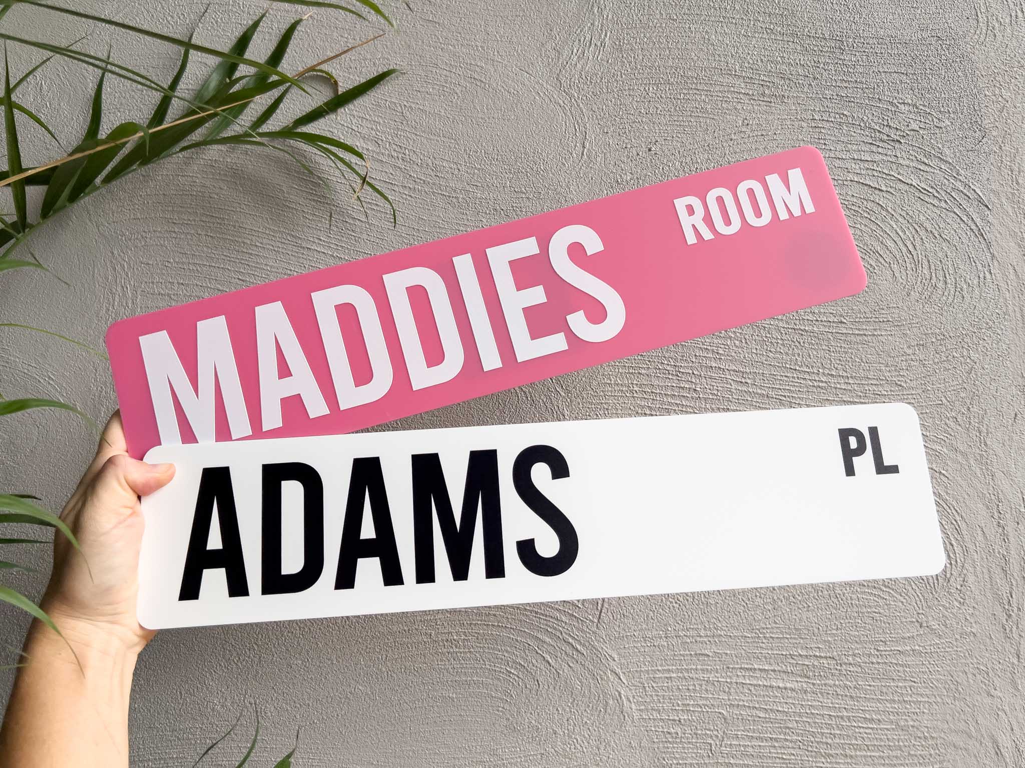 Classic customisable acrylic street signs in pink and white that read 'MADDIES ROOM' & 'ADAMS PL'.