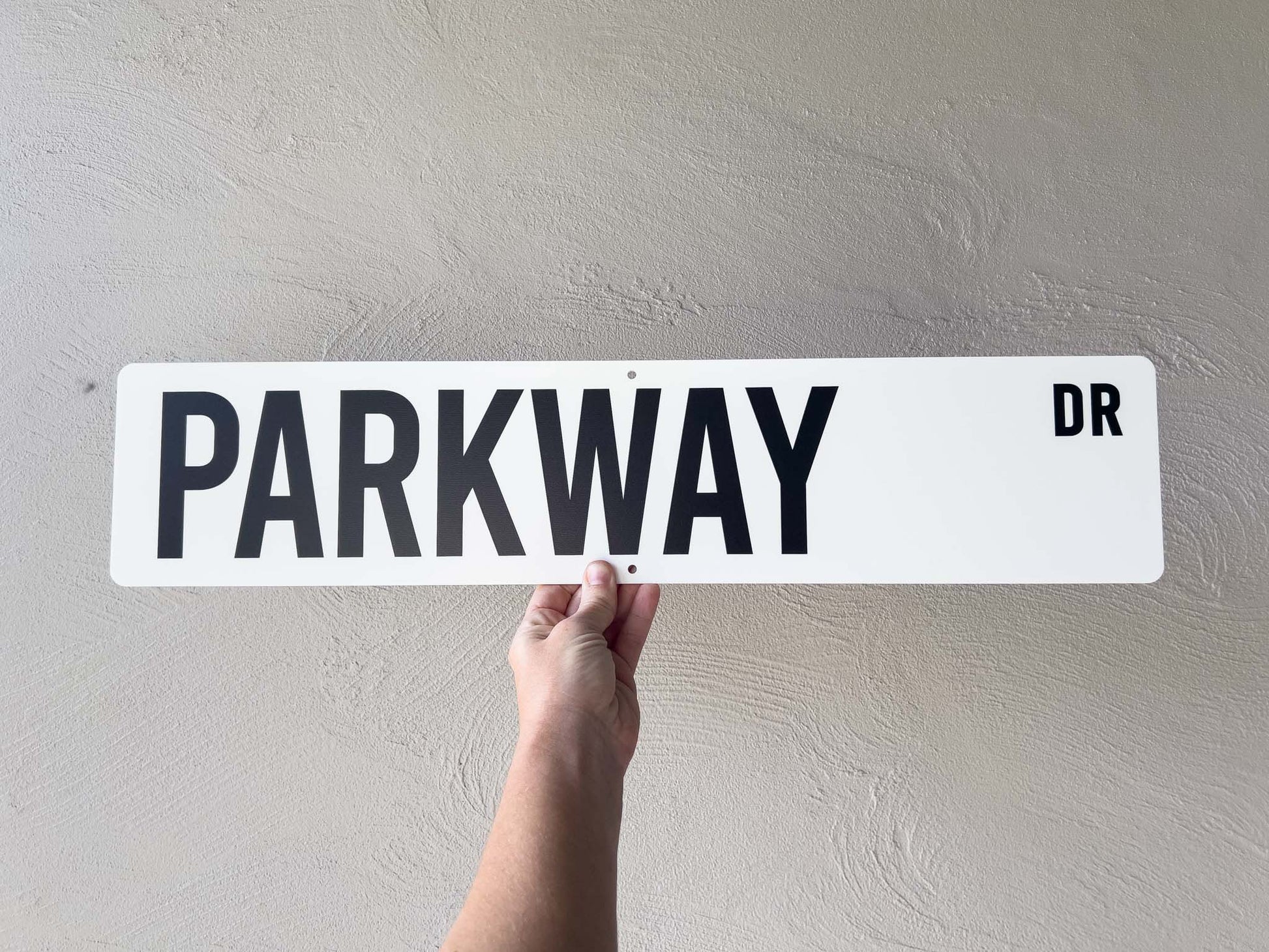 Hand holding a street sign with 'PARKWAY DR' text against a plain background
