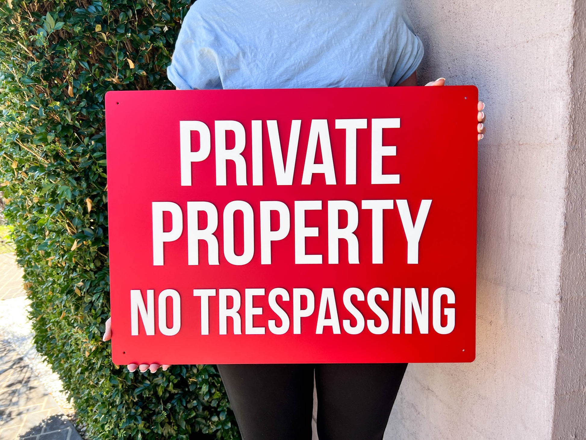 Person holding a red 'Private Property No Trespassing' sign outdoors.