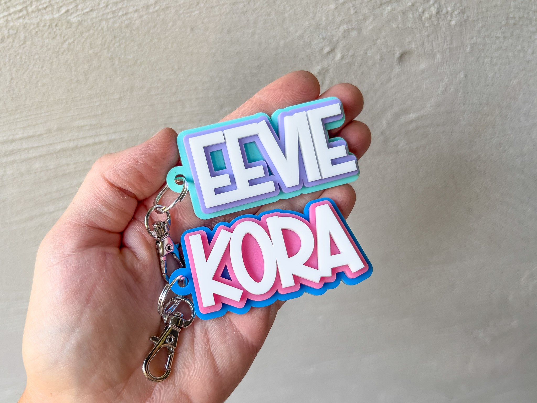 Colorful keychain with 'EEVIE KORA' text held in a hand against a neutral background