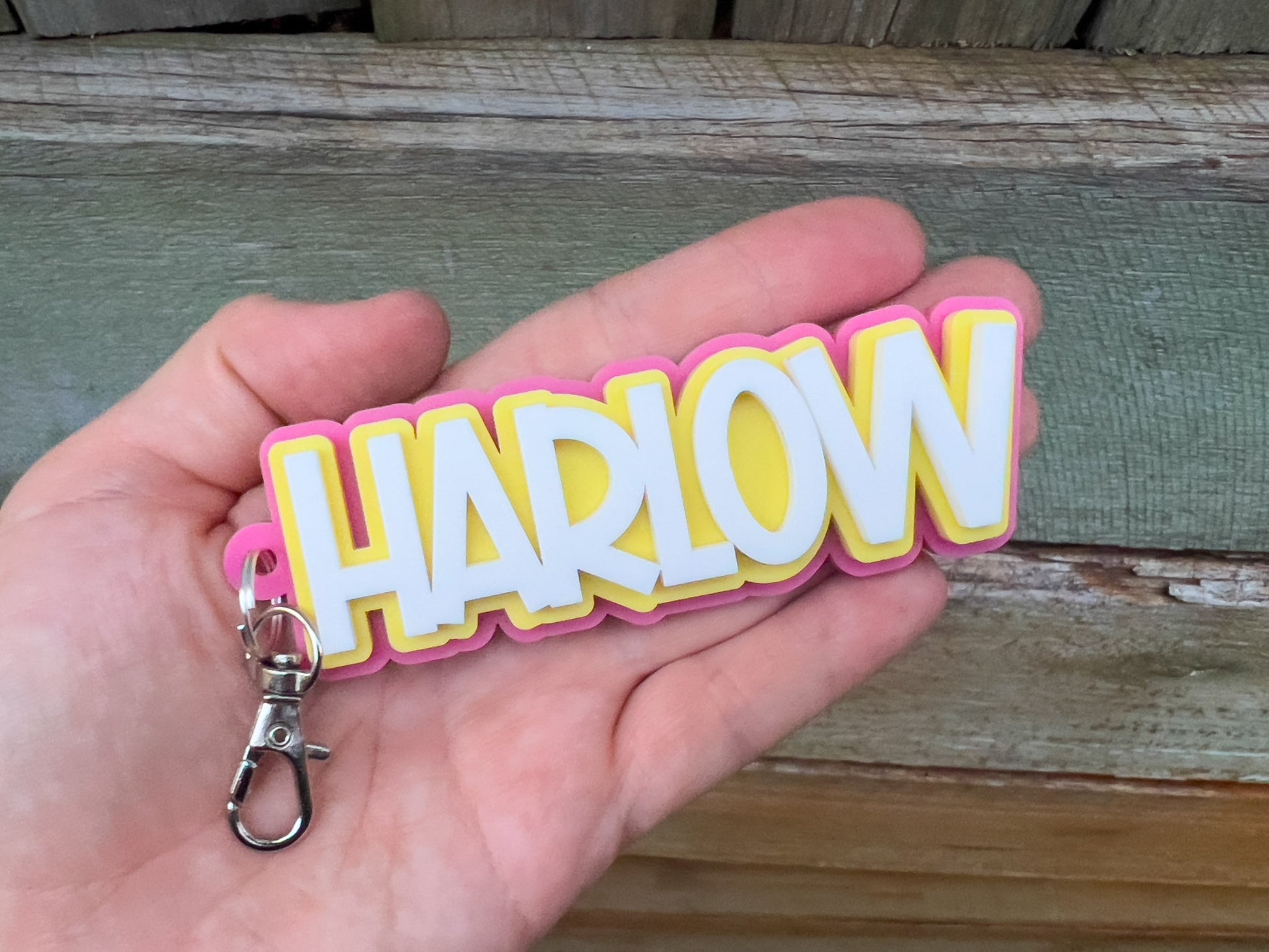 Keychain with 'HARLOW' text held in a hand against a wooden background