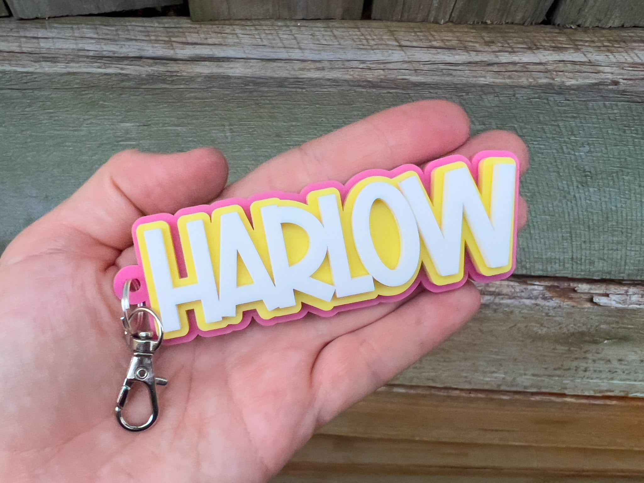 Keychain with 'HARLOW' text held in a hand against a wooden background