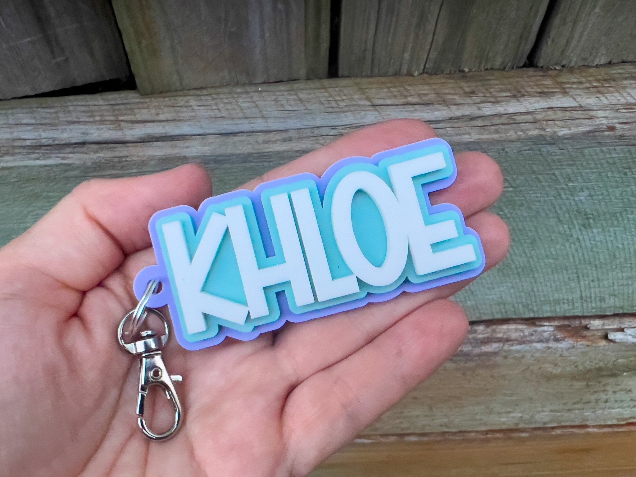 Keychain with 'KHLOE' in pastel colors held in a hand against a wooden background