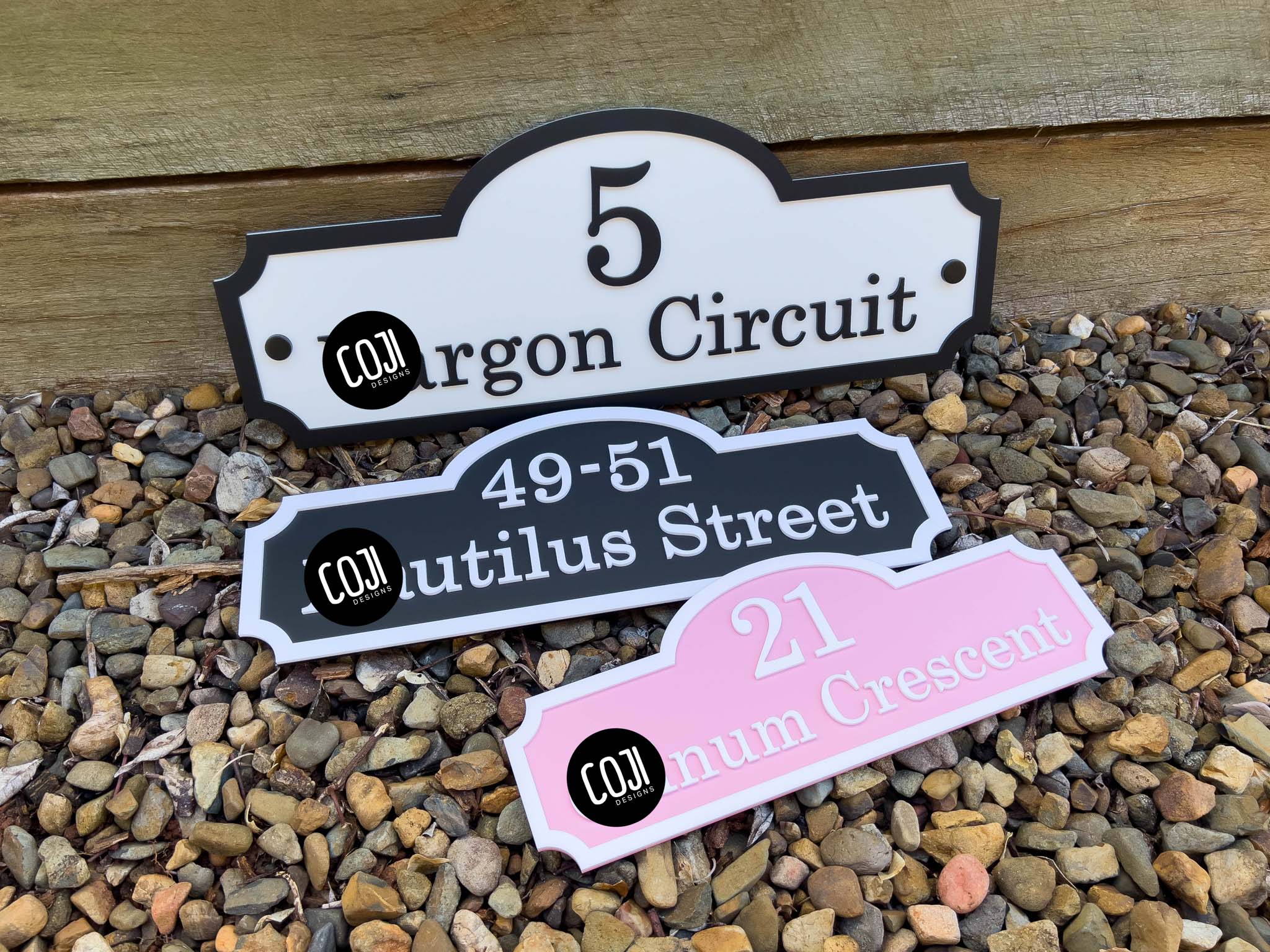 Three decorative vintage house number signs on a bed of small stones.