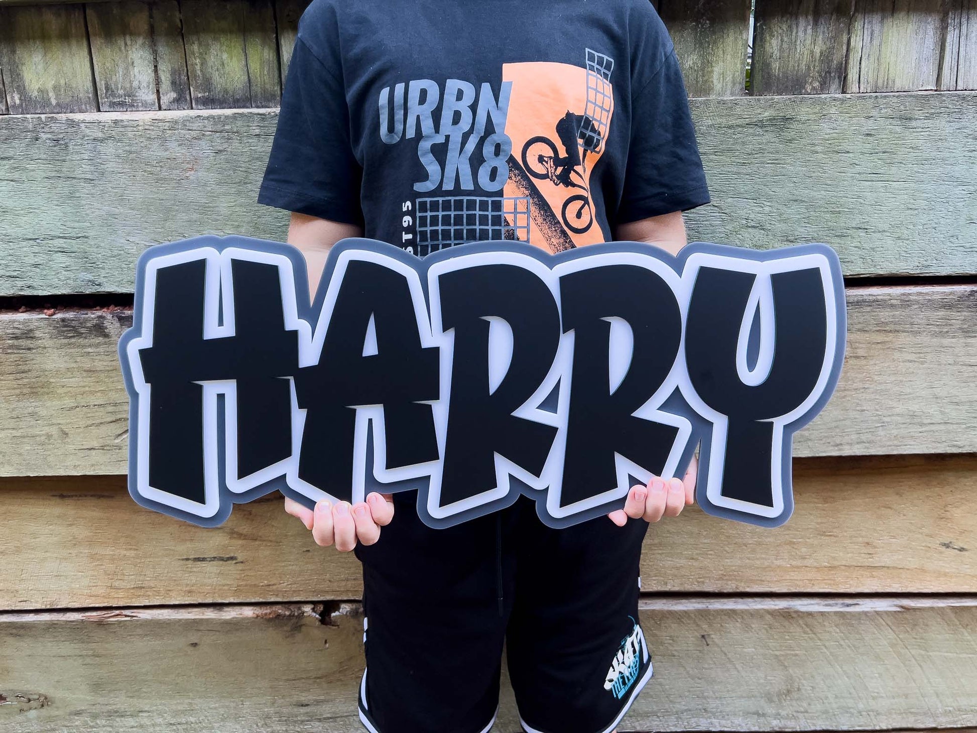Child holding a custom made 3D acrylic sign that says 'HARRY' in black, white and grey.